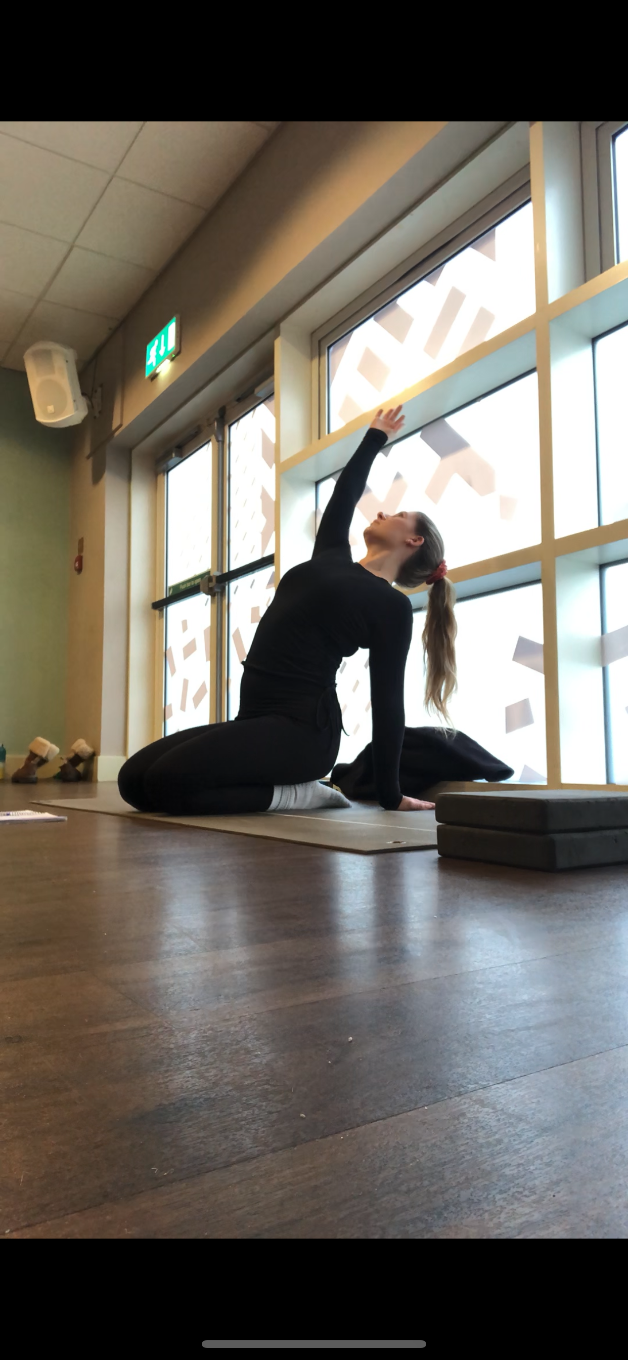KATHERINE IS SITTING ON HER HEELS, WITH ONE HAND BEHIND HER BACK AND THE OTHER EXTENDED OVERHEAD AS SHE PERFORMS A GENTLE BACKBEND DURING HER VINYASA FLOW.