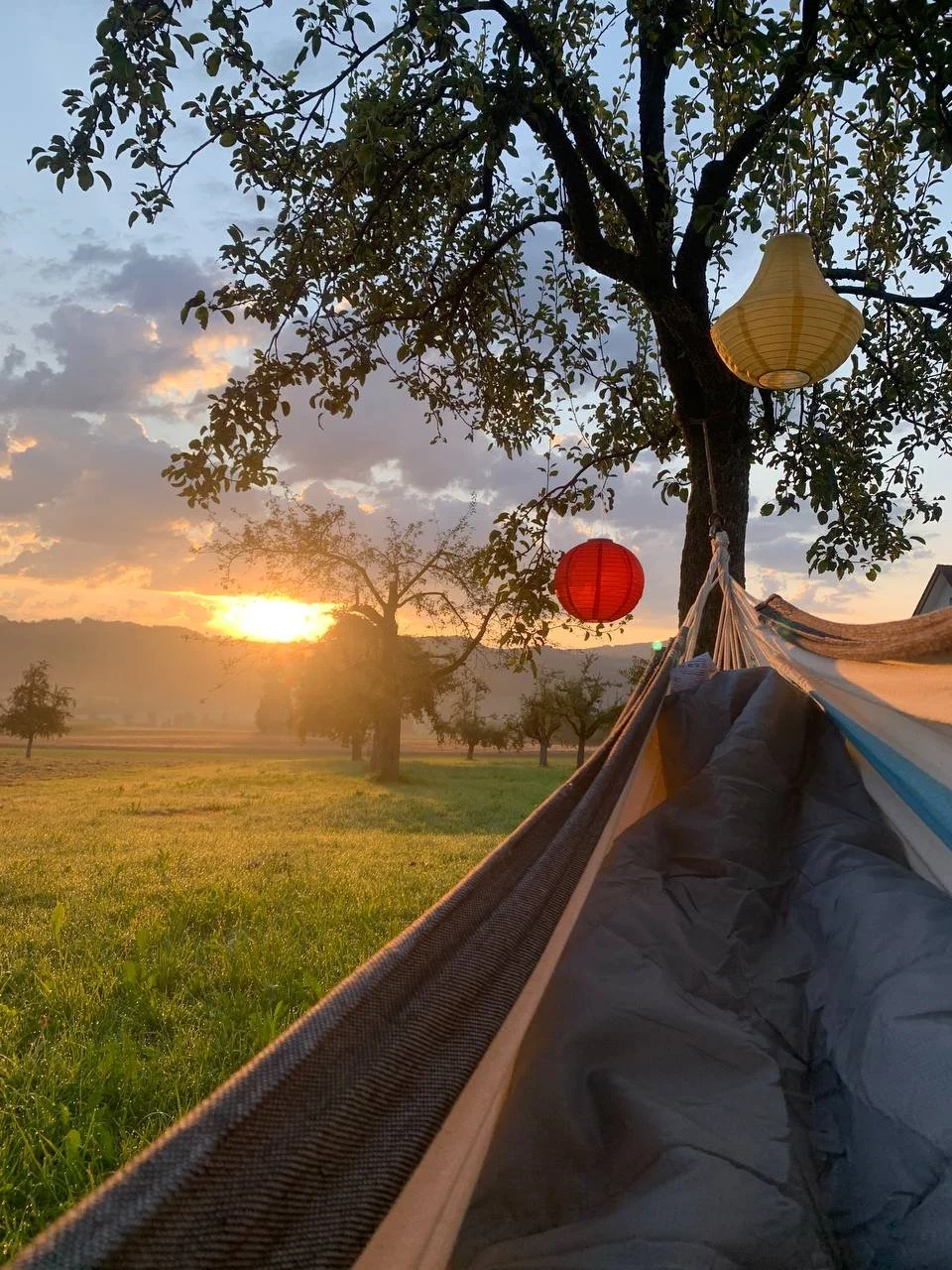 Pfadfinderzelt im Freien bei Sonnenuntergang mit bunten Papierlaternen und Baum im Hintergrund, an einer Wiese