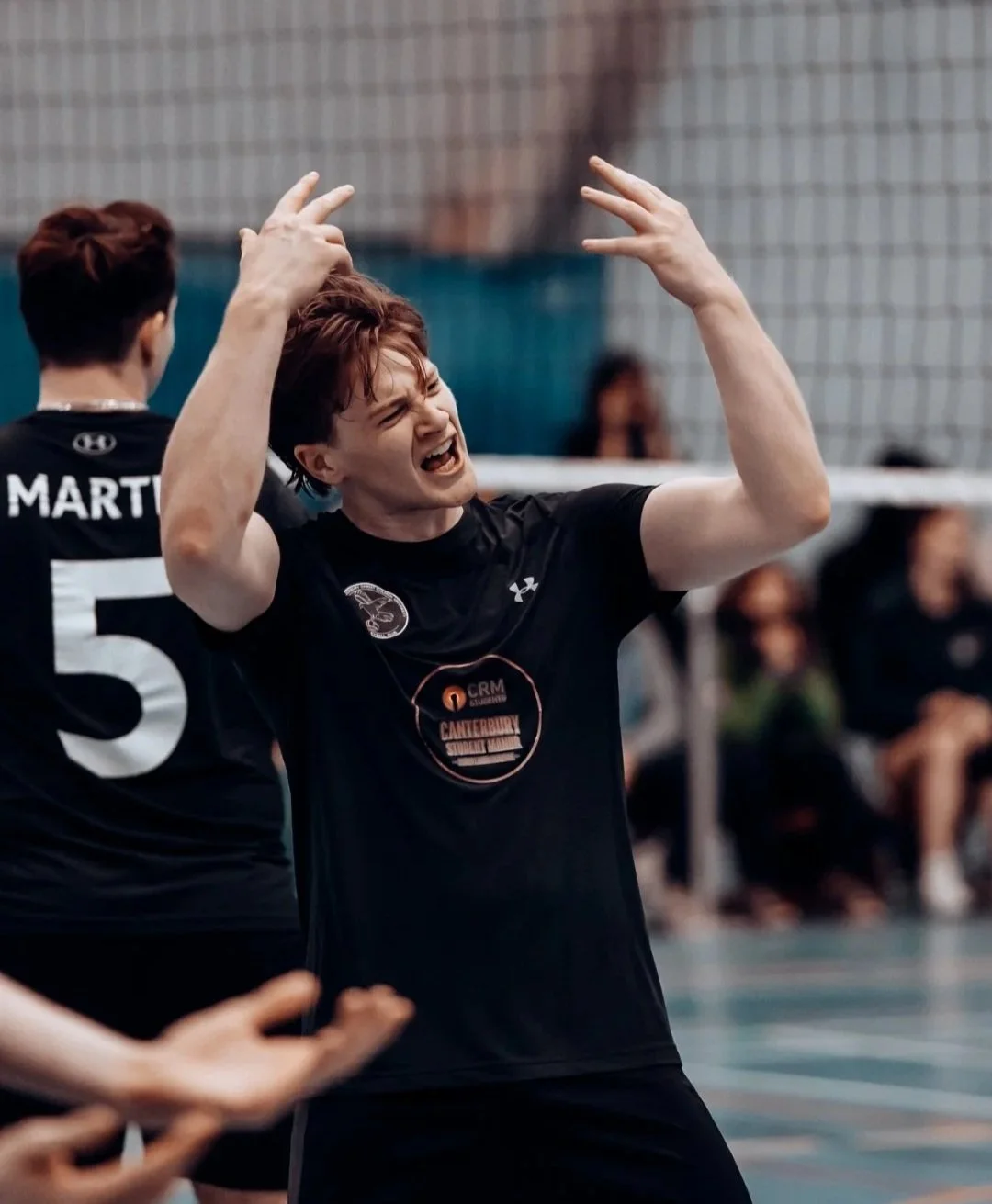 A woman in a black sports shirt appears frustrated or upset during a volleyball game, with her mouth open and hands raised.