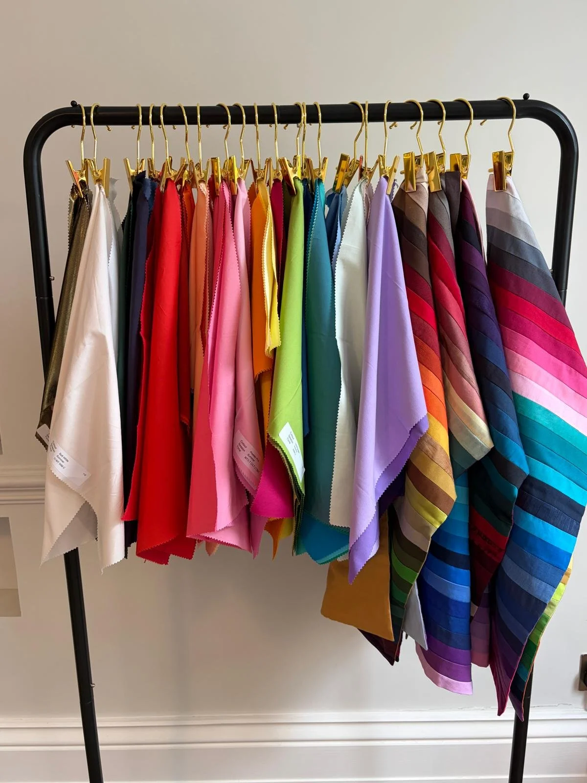 Colorful fabric drapes used for colour analysis hanging on a black metal rack, arranged from white to multicolored striped fabrics.