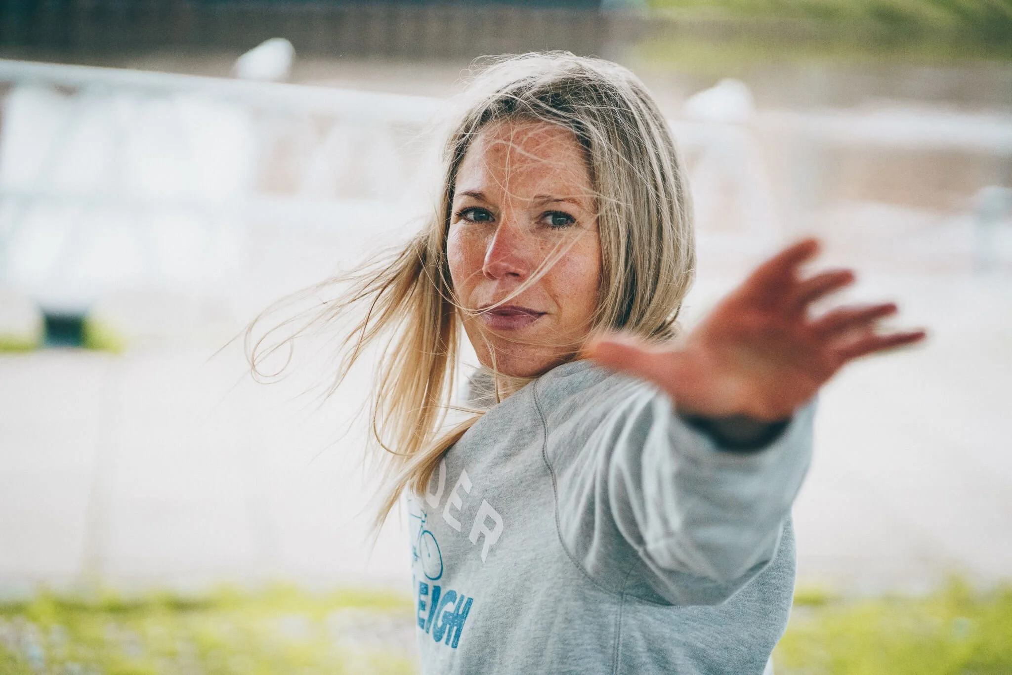 An image of Abi Adams from the waist up, her arm is outstretched towards the camera, and she is looking towards the camera
