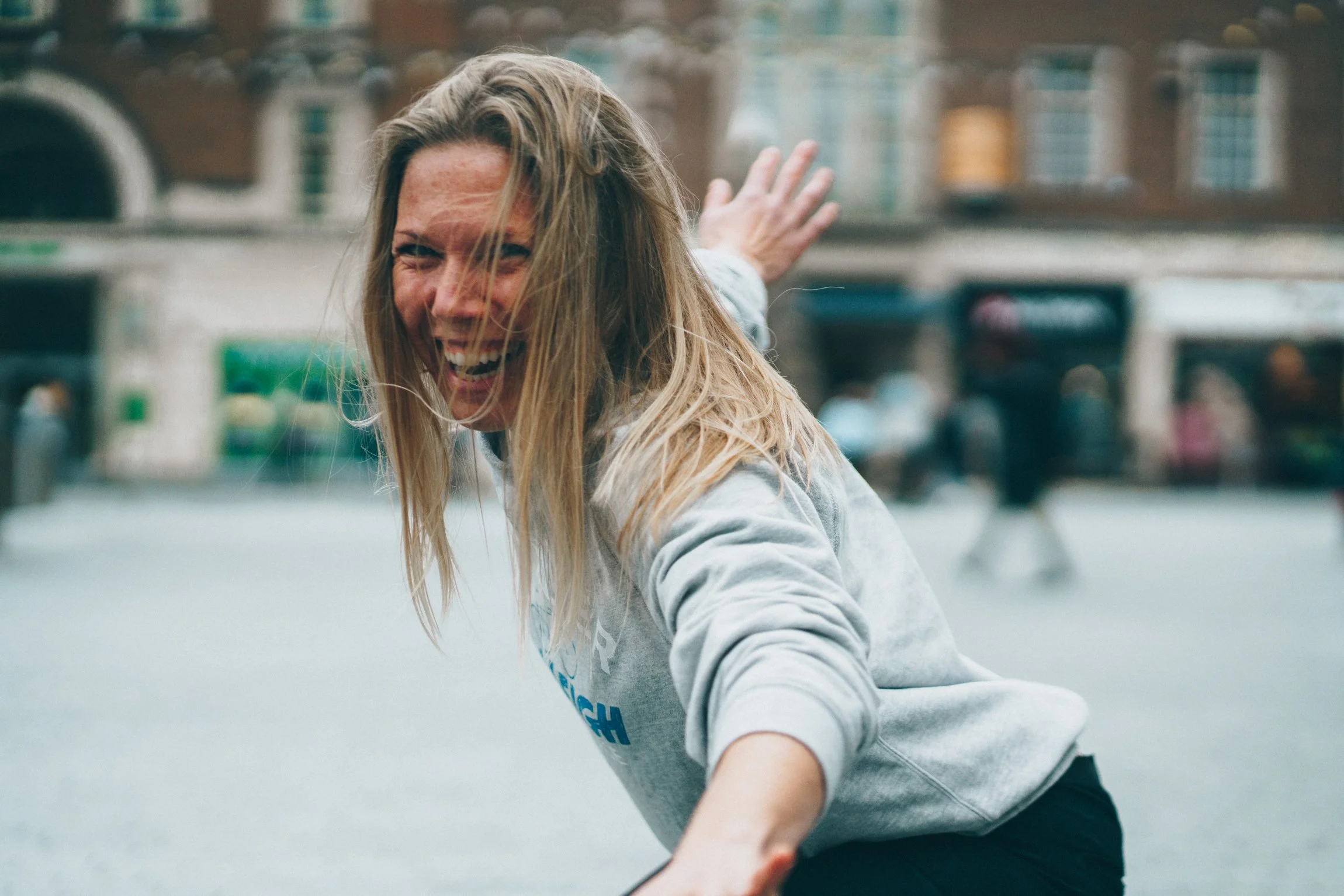 Abi Adams is crouched with her arms outstretched, she is looking towards the camera and laughing.