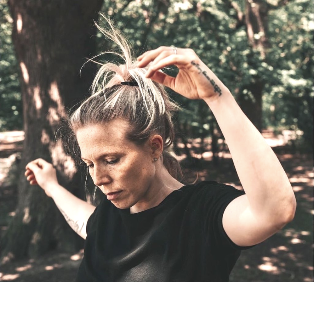 Abi Adams is surrounded by trees, her eyes are closed and her arms are up.