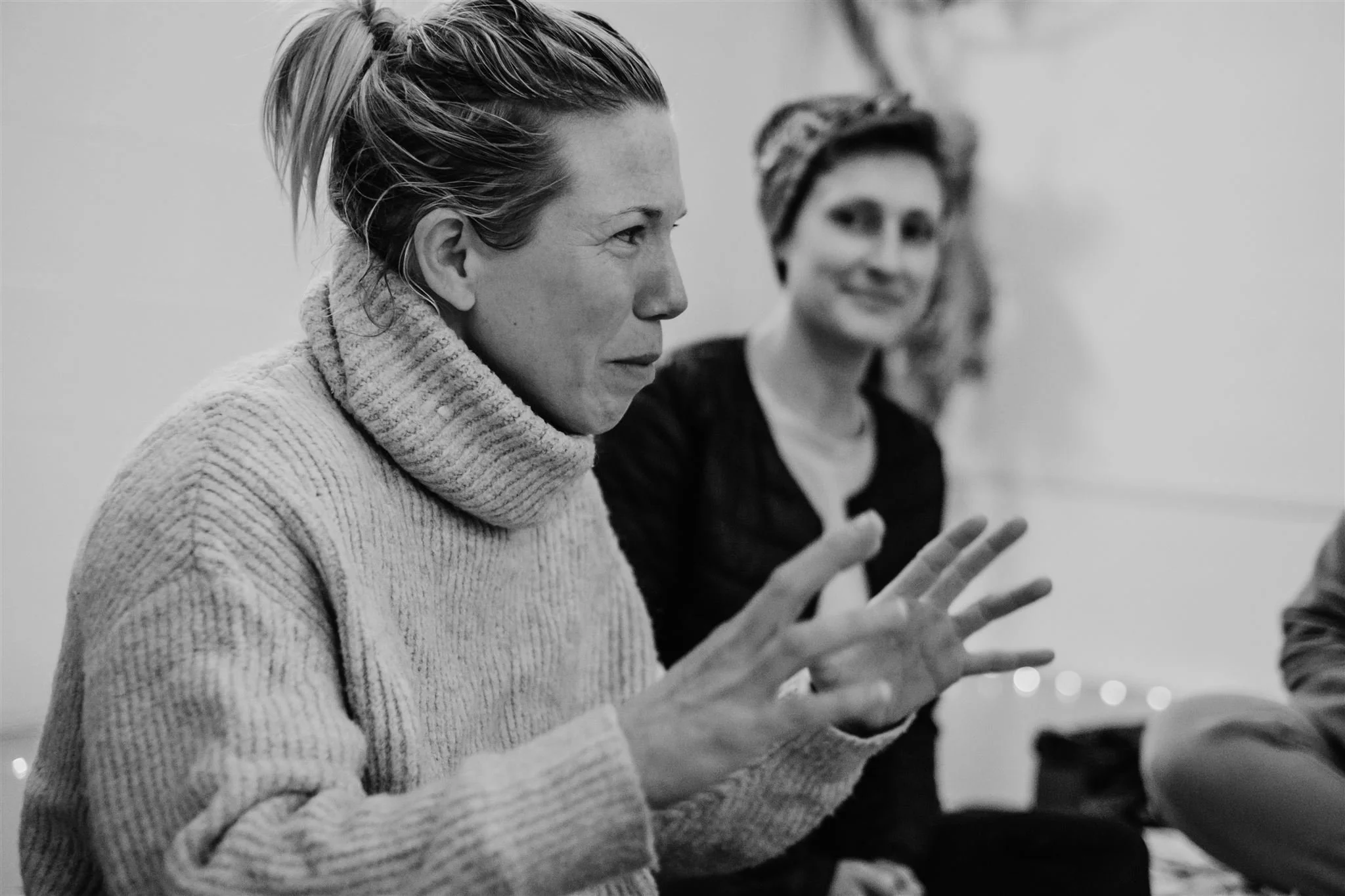 Abi Adams gesturing with her hands, whilst another woman in the background is smiling and looking at her.