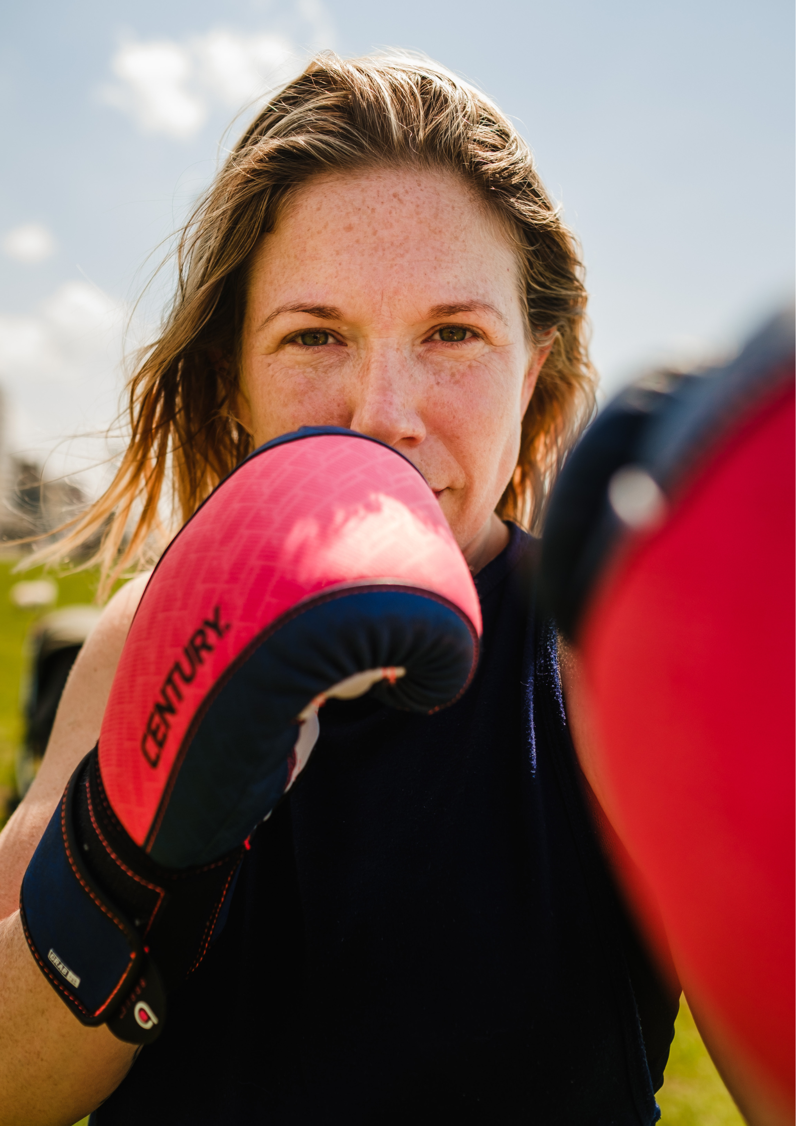 Abi Adams has pink and black boxing gloves on, and is punching one arm towards the camera, with the other boxing glove partially covering her face.