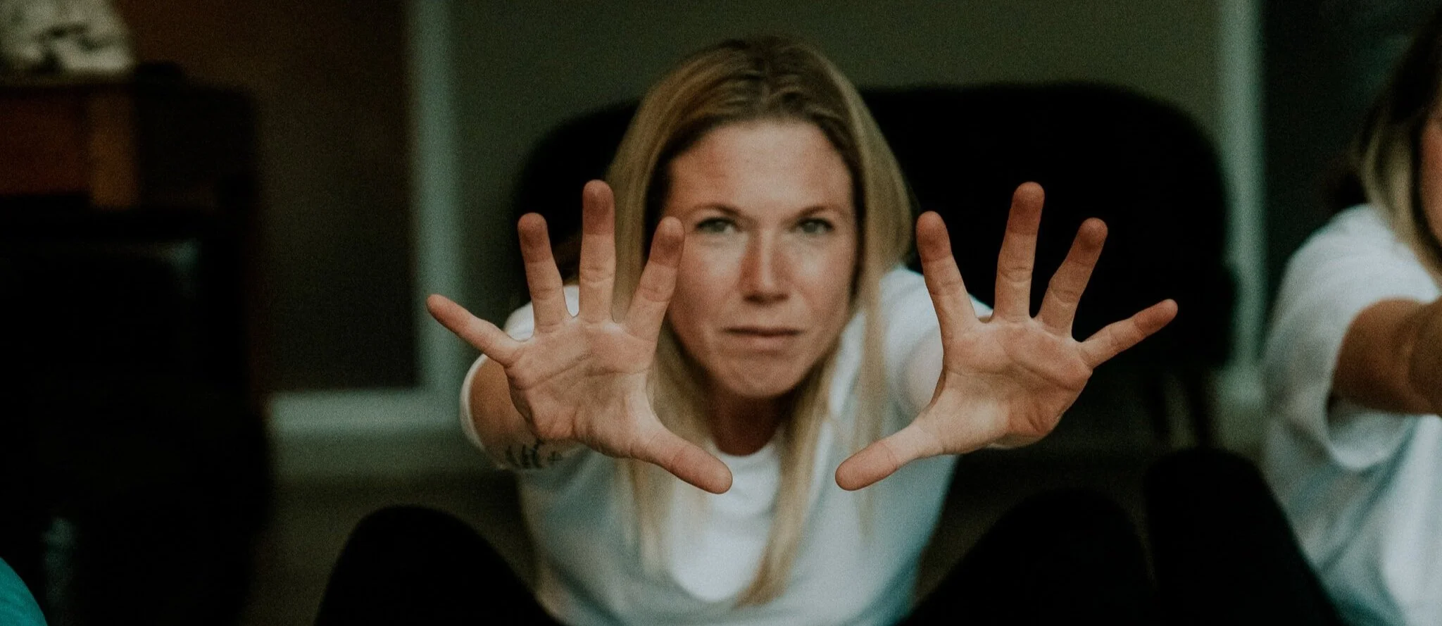 Abi Adams is crouched down and reaching her arms and hands towards the camera.
