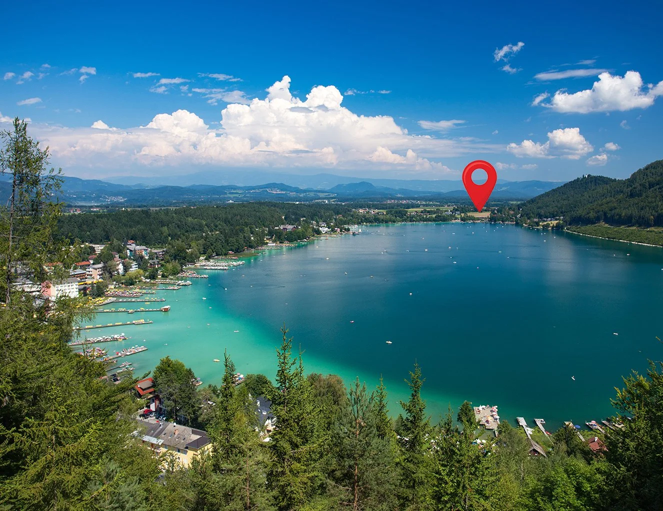 A scenic view of a lake surrounded by green trees and hills under a partly cloudy sky.