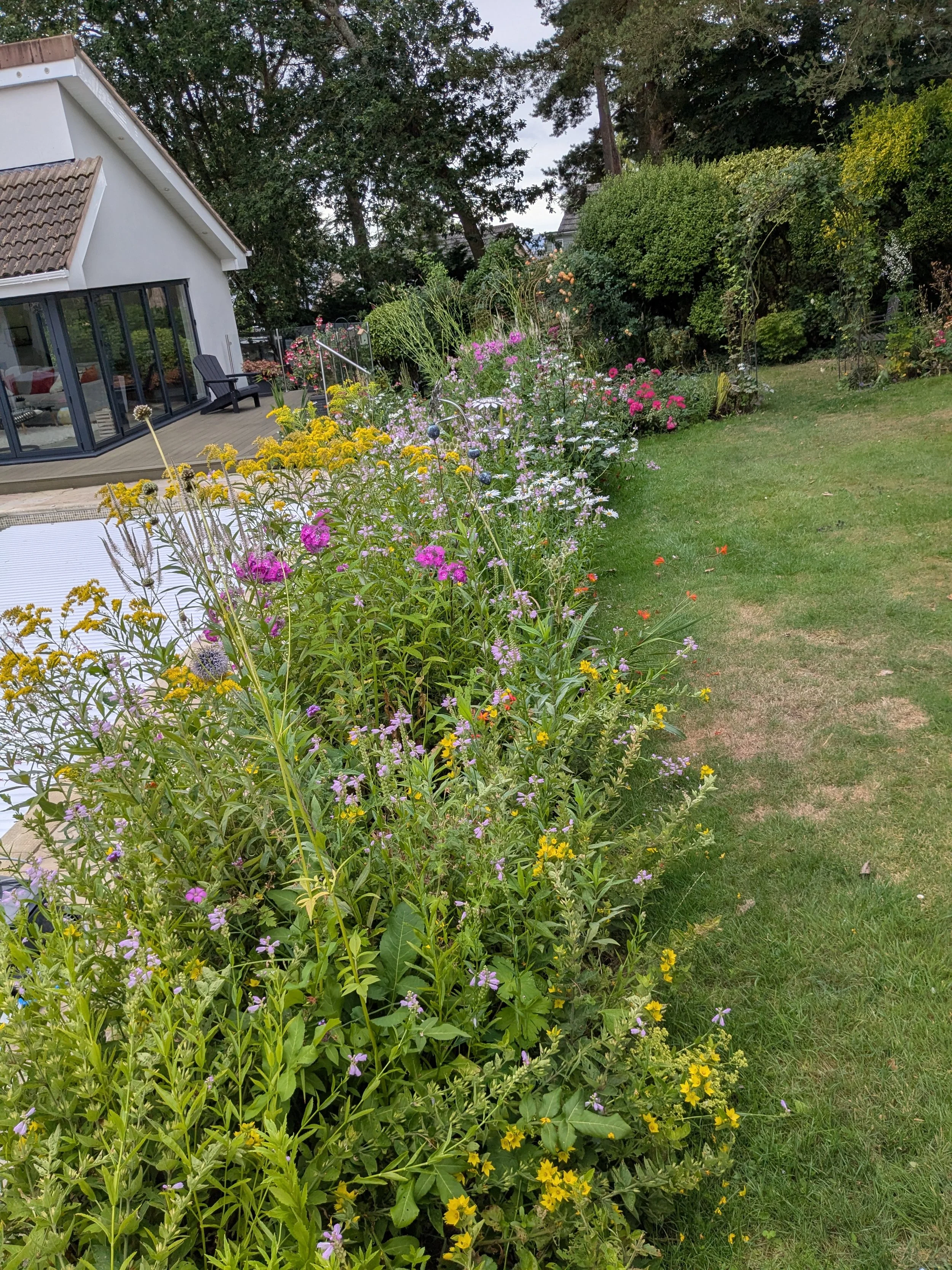 Colorful flower garden next to a modern house with sliding glass doors and outdoor seating.