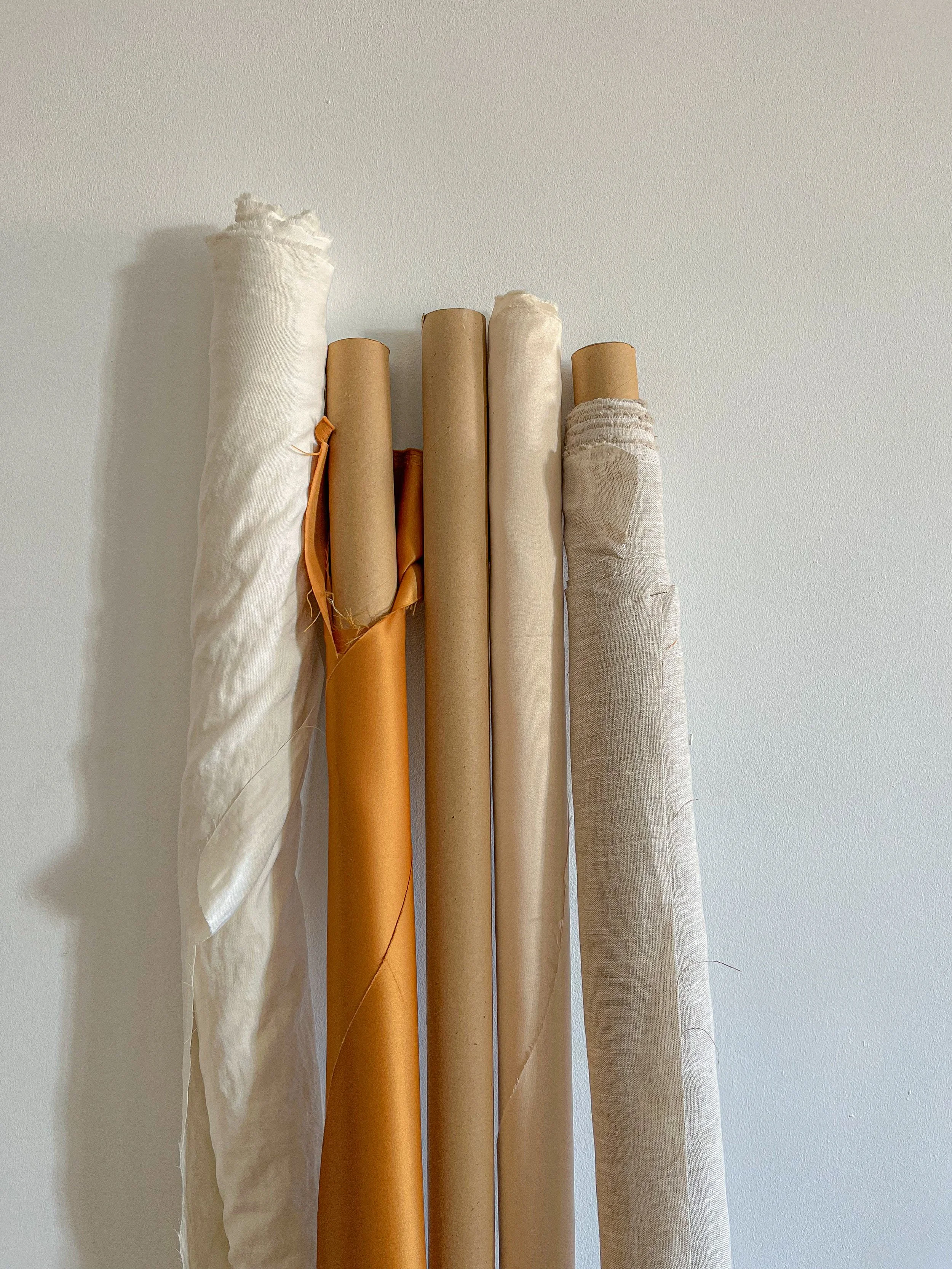 Vertical rolls of different fabrics and papers on a white wall.