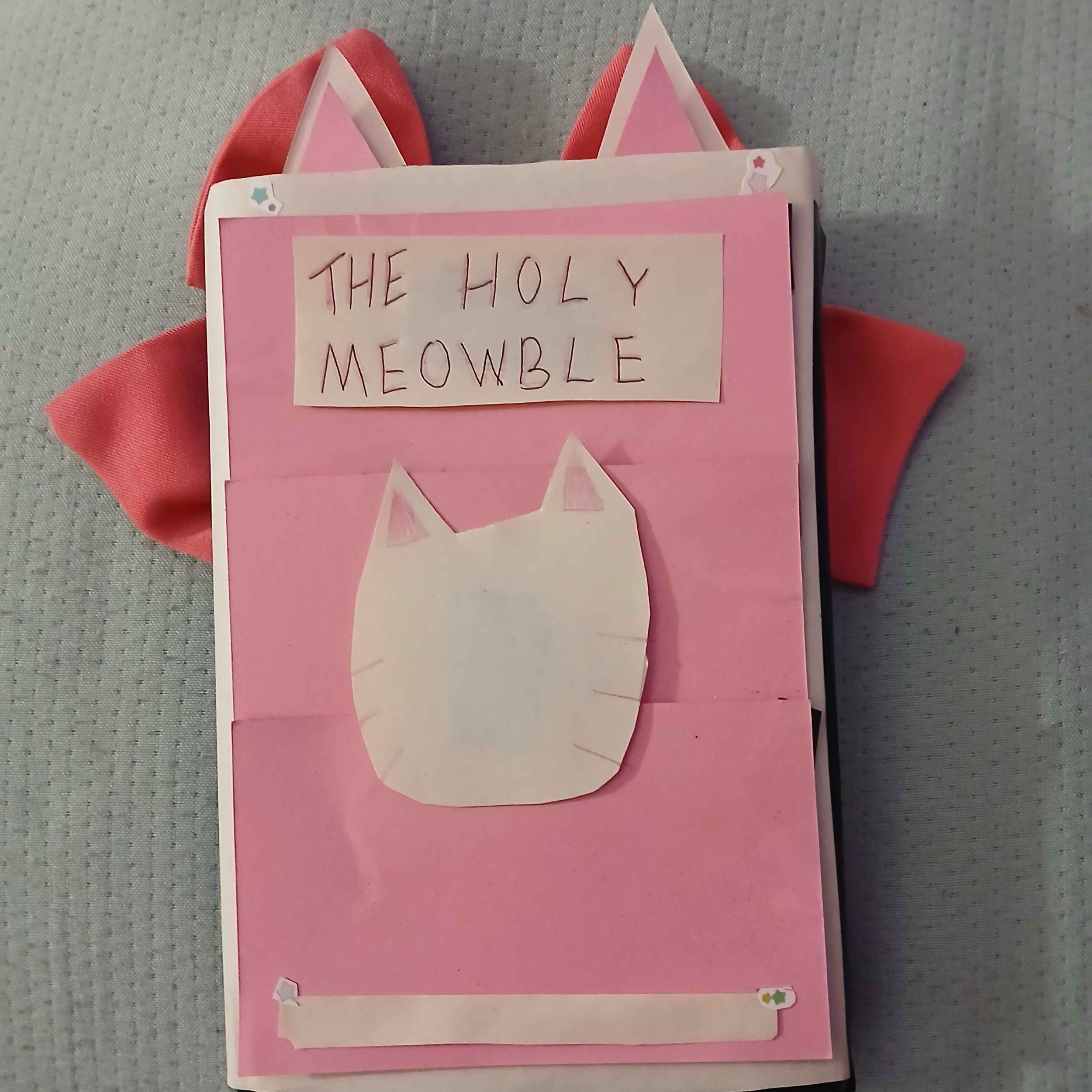 'The Holy Meowble.' Decorated with pink and red ribbons and small star stickers.