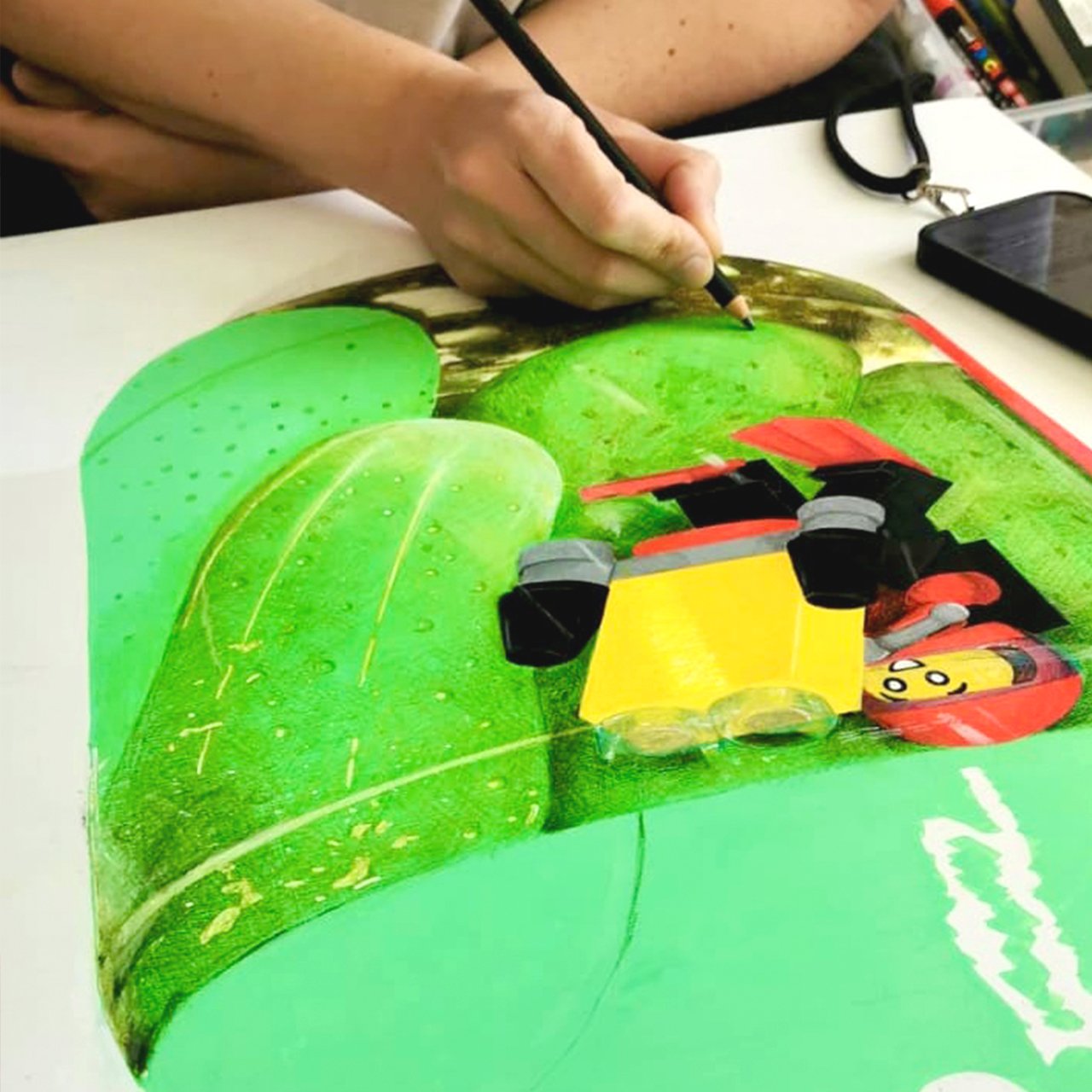 Person coloring a LEGO-themed image with a green background, leaves, and LEGO character illustration.