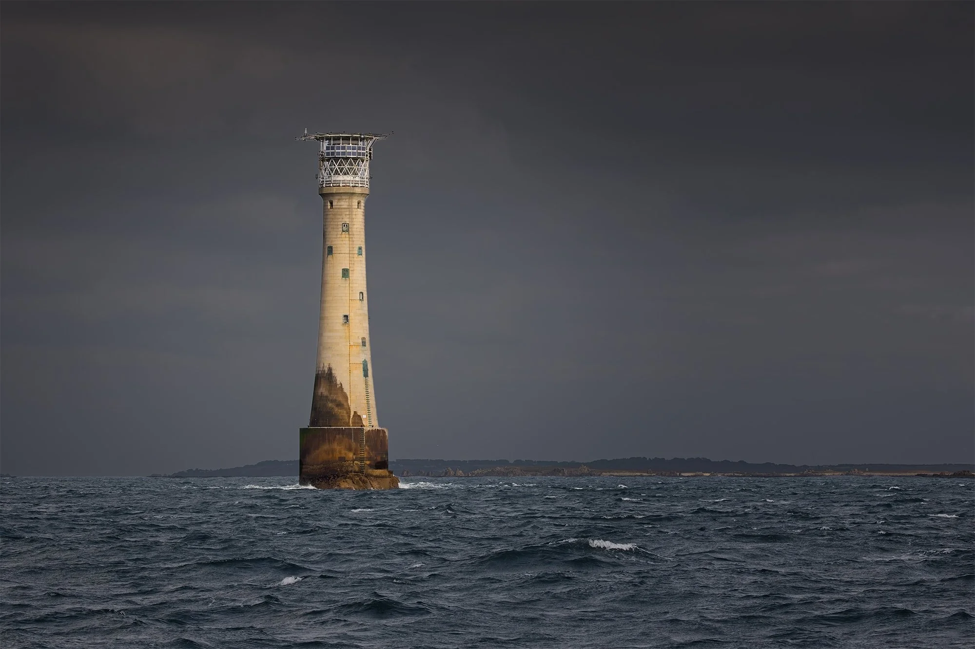A lighthouse standing on a rocky base in the ocean, with dark clouds in the sky.