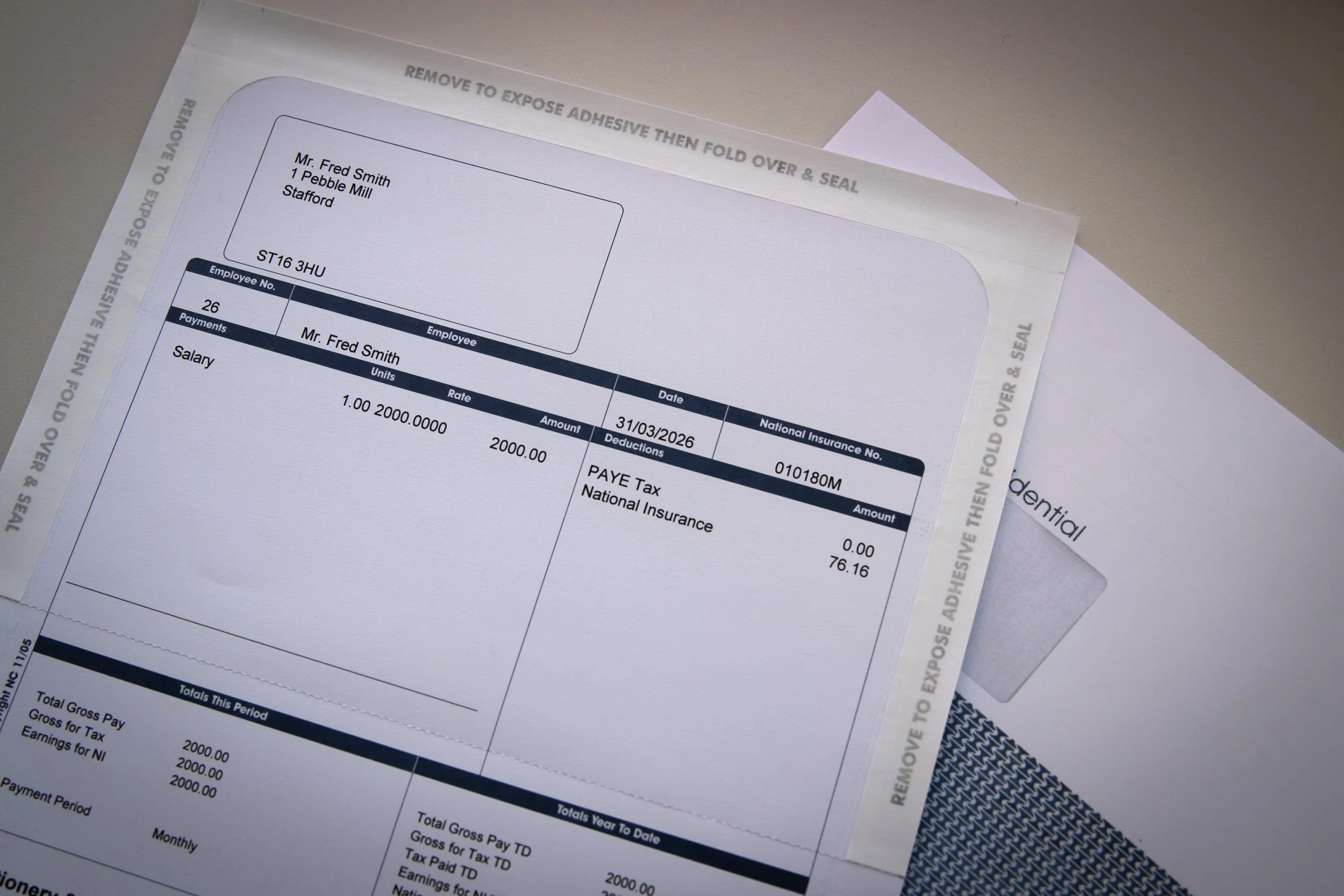 A payroll slip for Mr. Fred Smith showing salary details, deductions, and total pay information, with a partially visible envelope in the background.