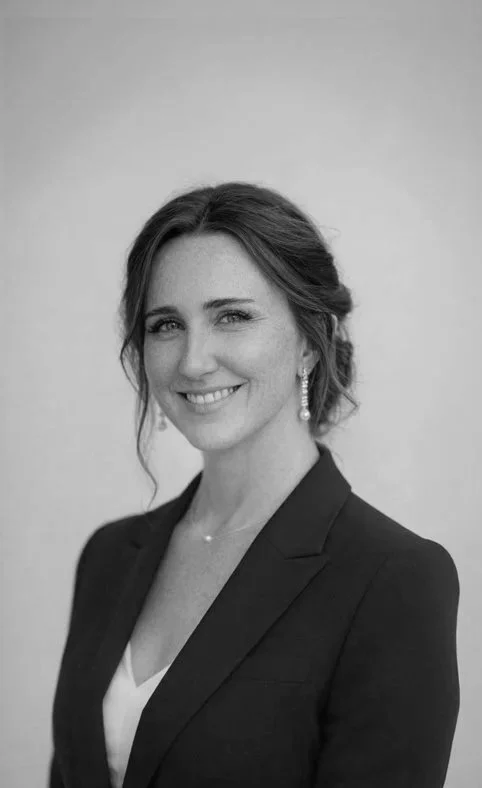 Black and white portrait of a woman with shoulder-length hair, wearing earrings, a blazer, and a necklace, smiling at the camera.