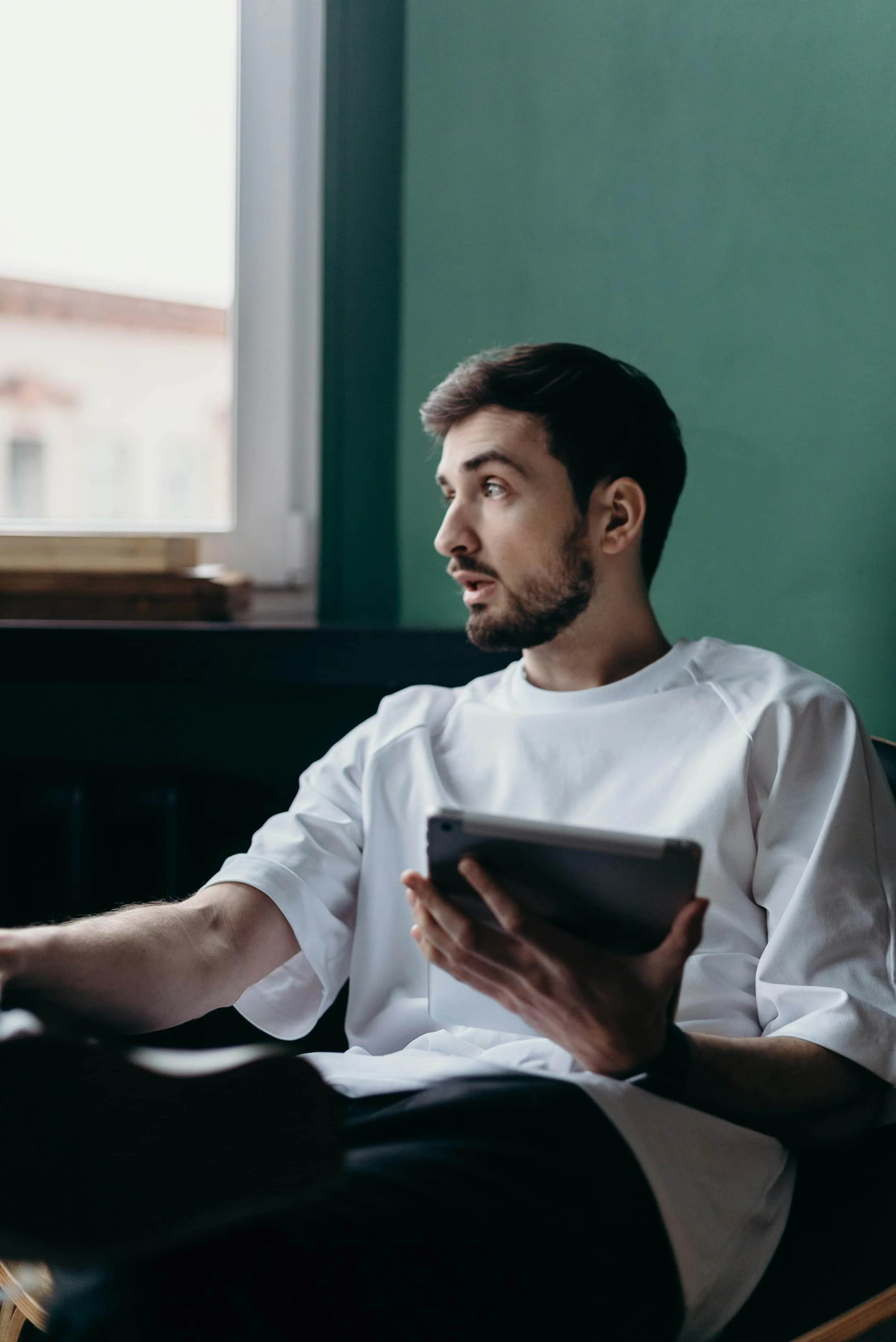 A man sitting in a chair holding a tablet and looking out the window, representing adult anxiety and trauma therapy at Inside Out Therapy in Peoria, AZ
