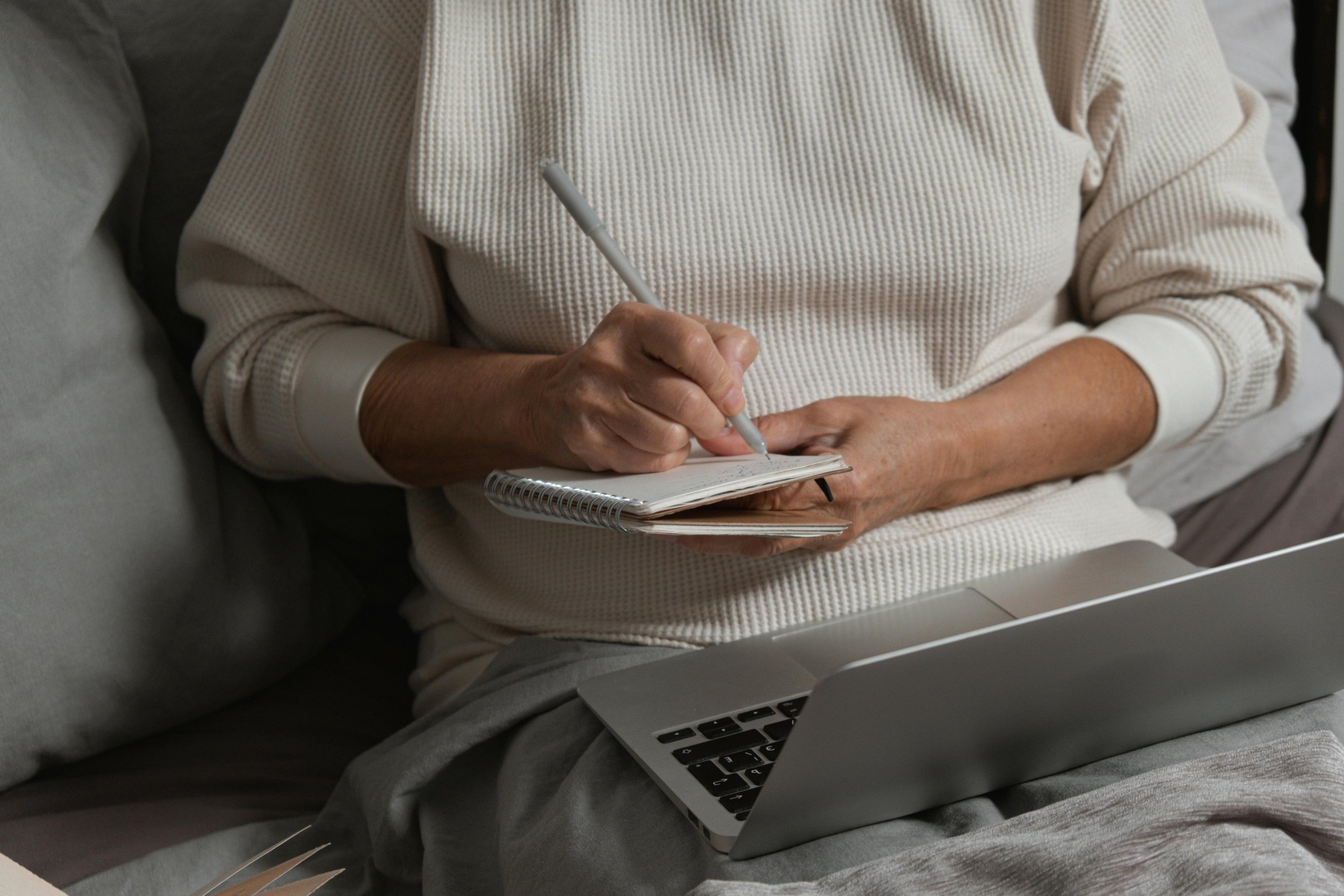 A person sitting on a couch writing in a notepad with a laptop open on their lap, representing the mental health blog at Inside Out Therapy and Consulting in Peoria, AZ