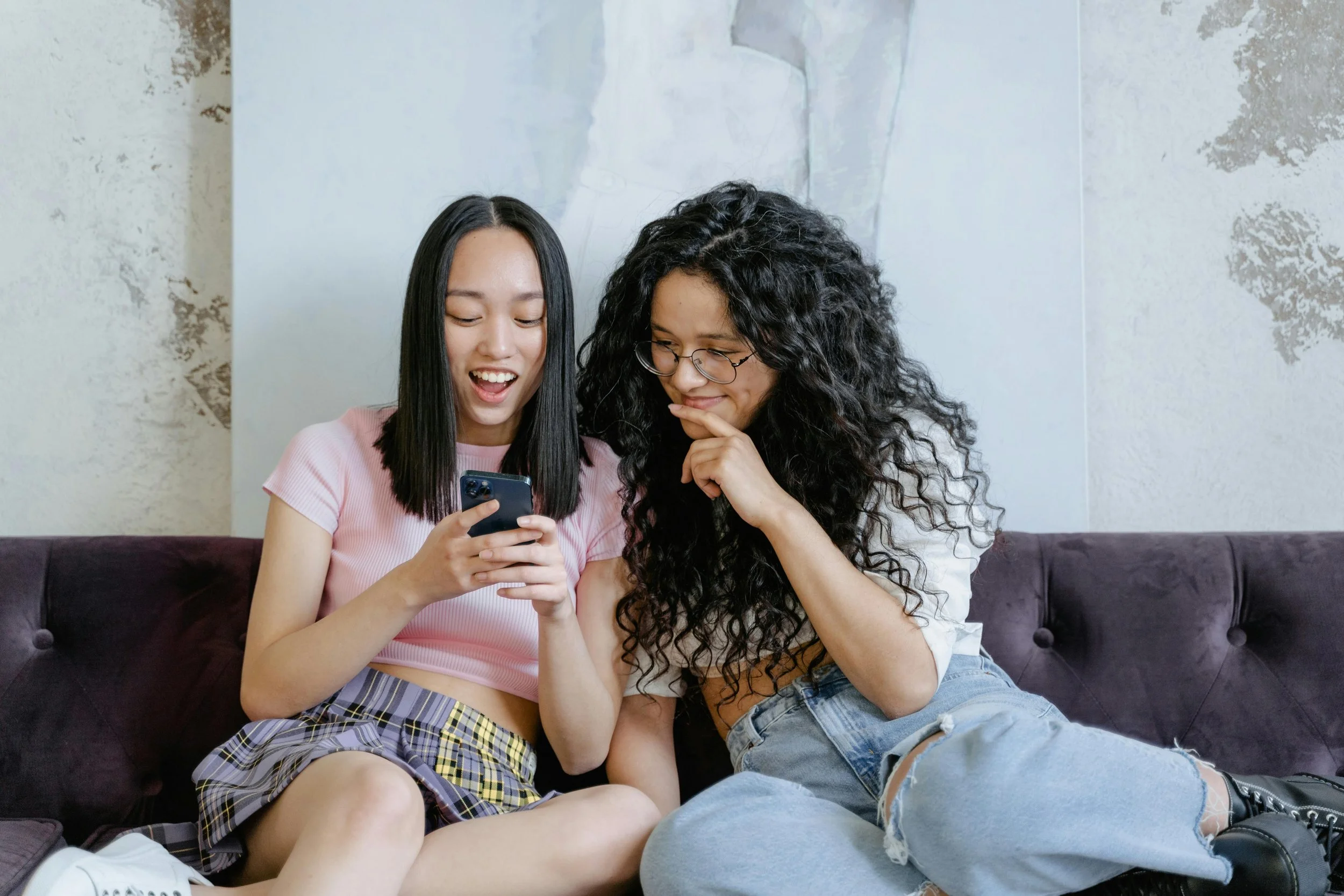 Two teenage girls sitting together looking at a phone, representing teen therapy and emotional regulation support at Inside Out Therapy in Peoria Arizona