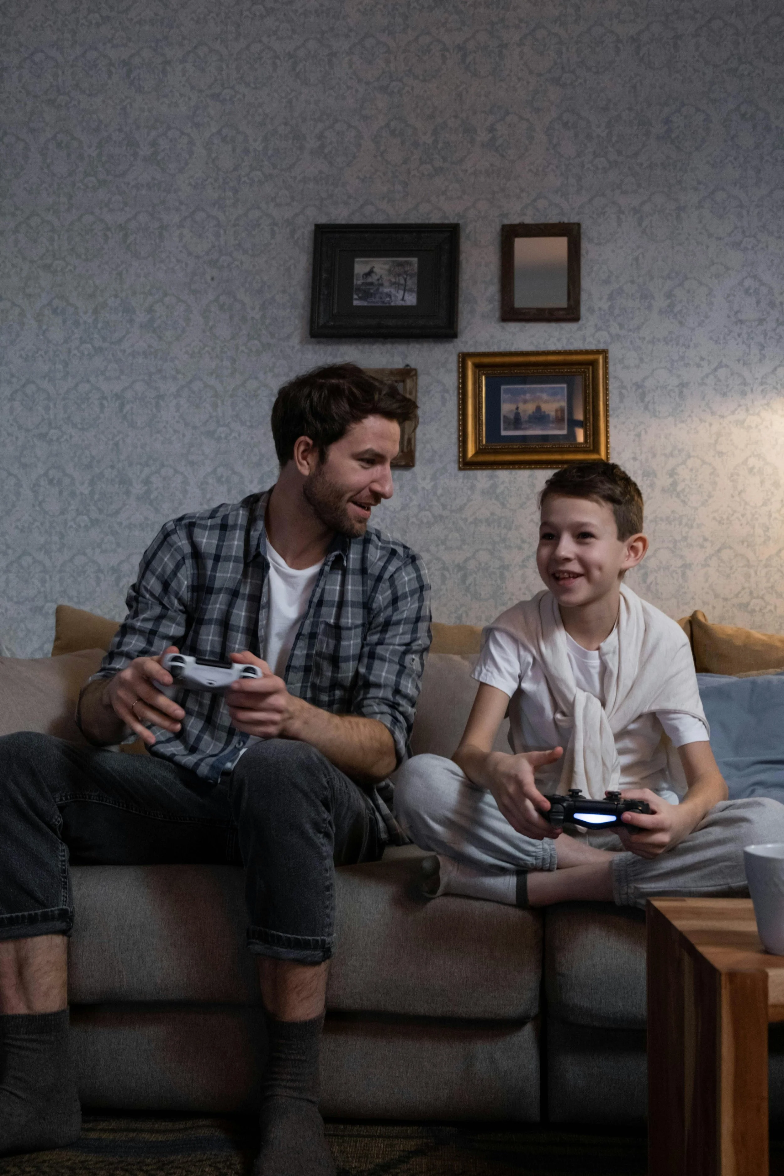 Father and son sitting together on a couch smiling while playing video games, representing child therapy and behavioral regulation support at Inside Out Therapy in Peoria Arizona