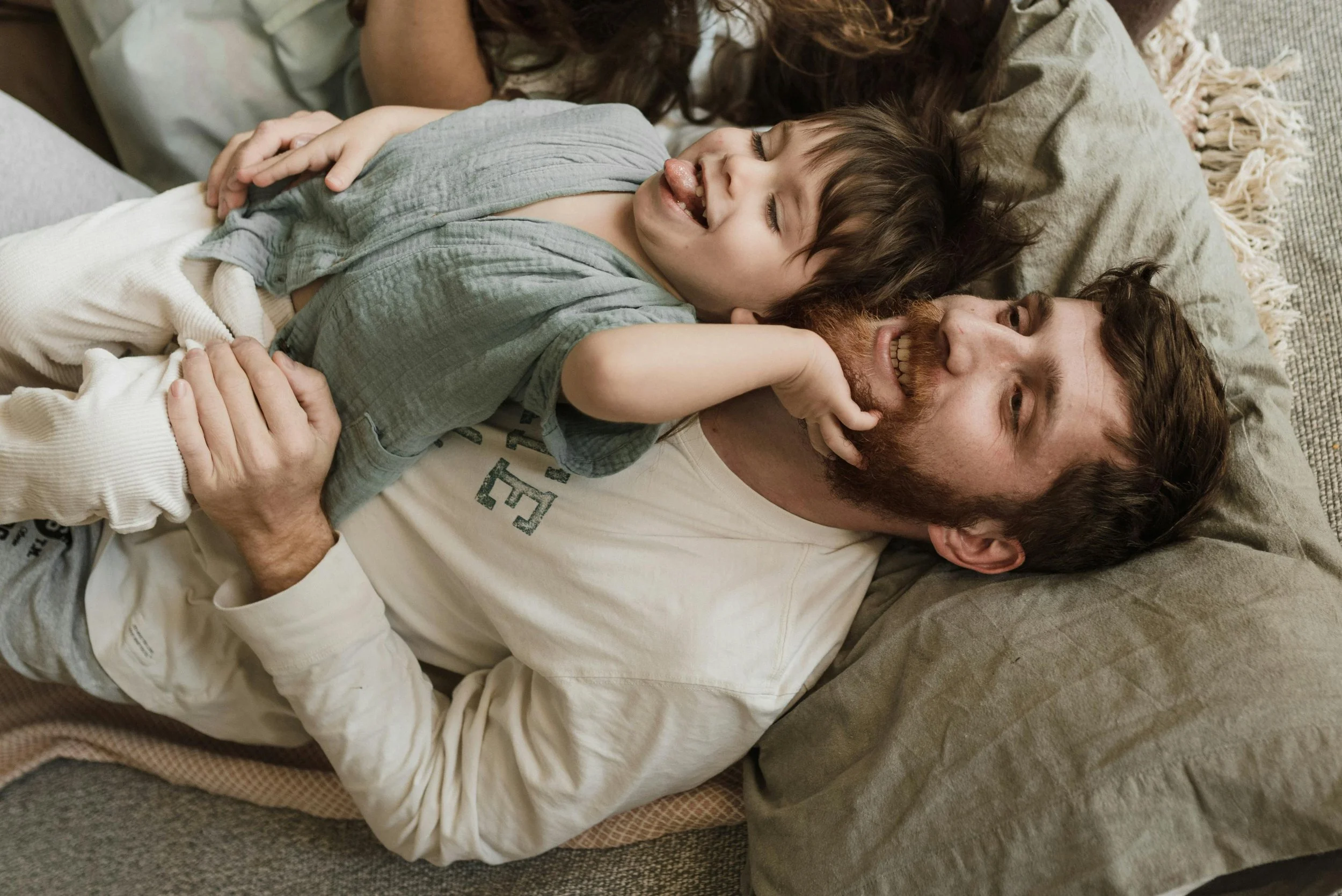 Father lying in bed with young son resting on top of him smiling, representing family connection and anxiety therapy at Inside Out Therapy in Peoria Arizona