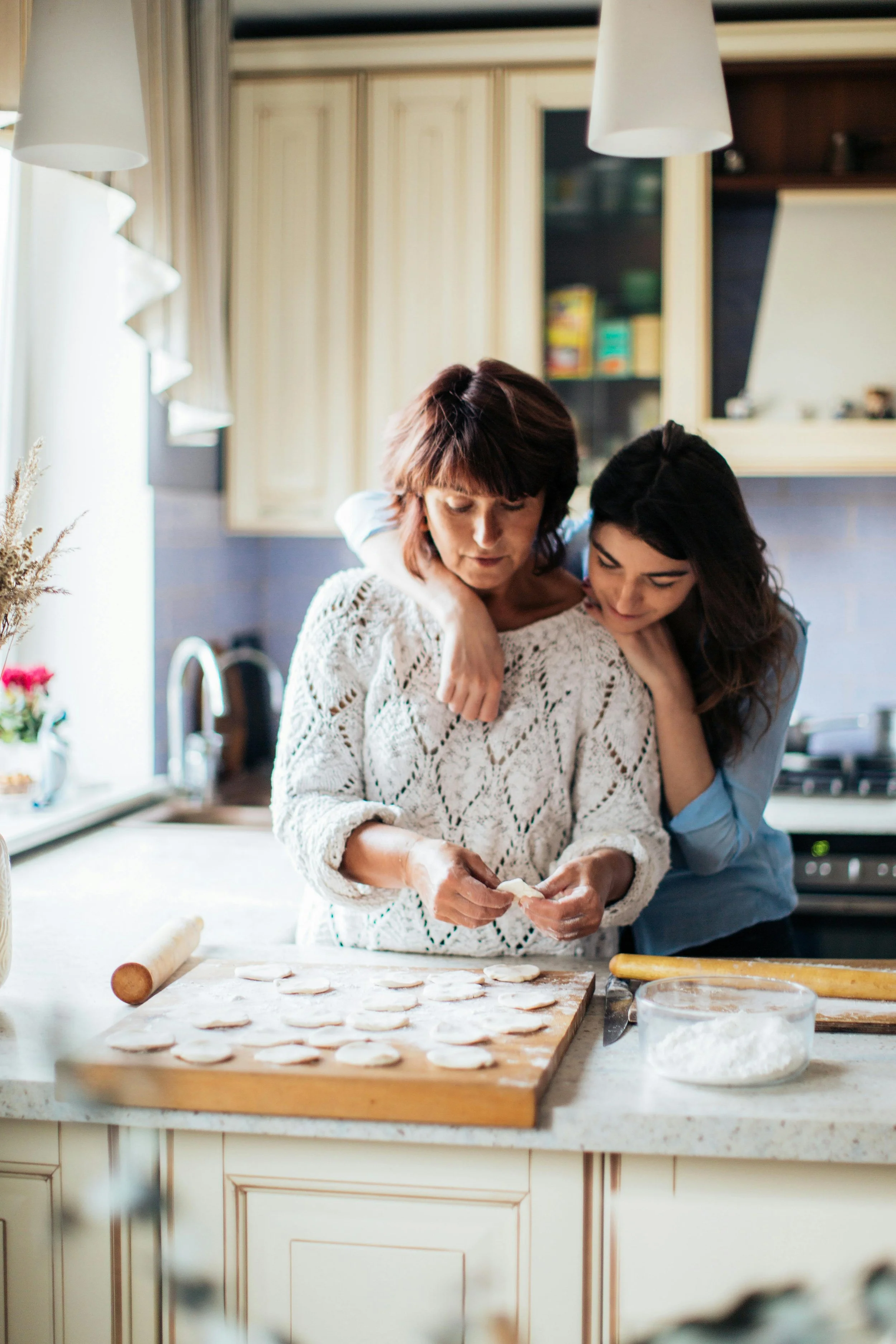 Teenage girl with arm around her mother while she prepares food in kitchen, representing attachment-based family therapy in Peoria Arizona