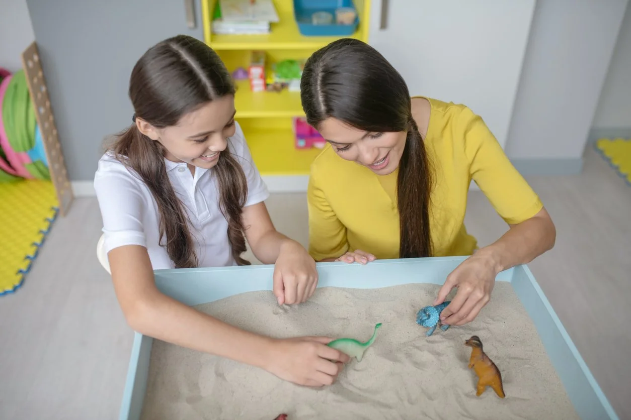 A child and therapist working together over a sand tray with small figures, representing sand tray therapy sessions at Inside Out Therapy and Consulting in Peoria, AZ