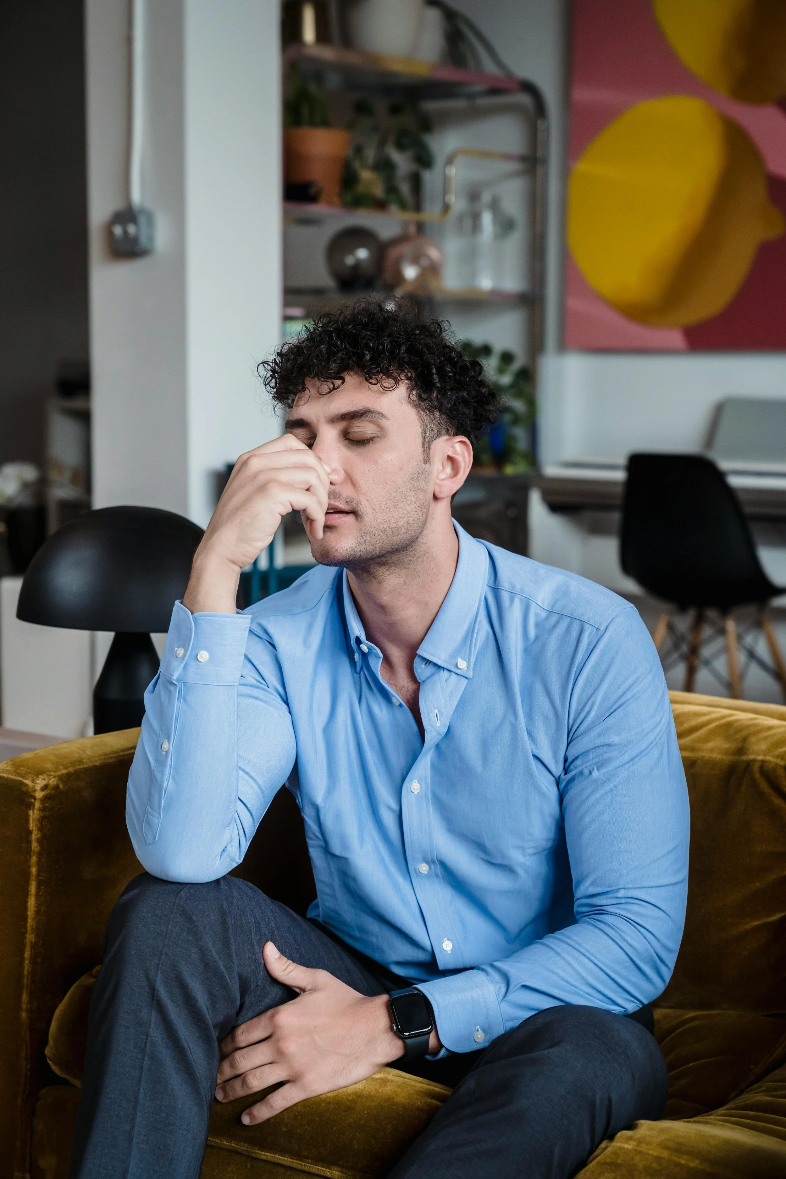 A man sitting on a couch with his eyes closed and hand on his face, representing adults seeking trauma therapy and EMDR treatment in Peoria, AZ