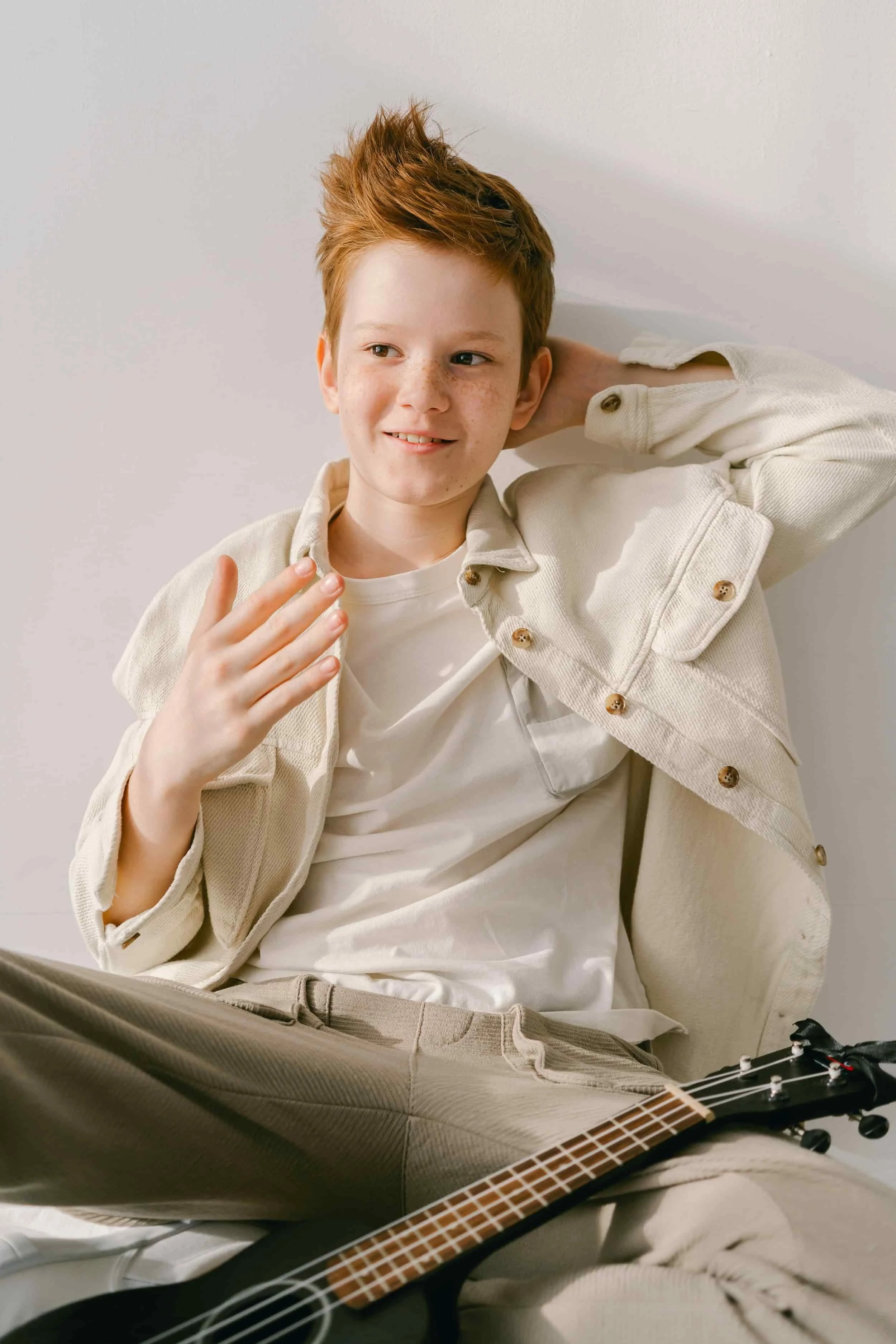 A smiling red-haired boy sitting relaxed with a ukulele, representing child therapy and emotional support in Peoria, AZ