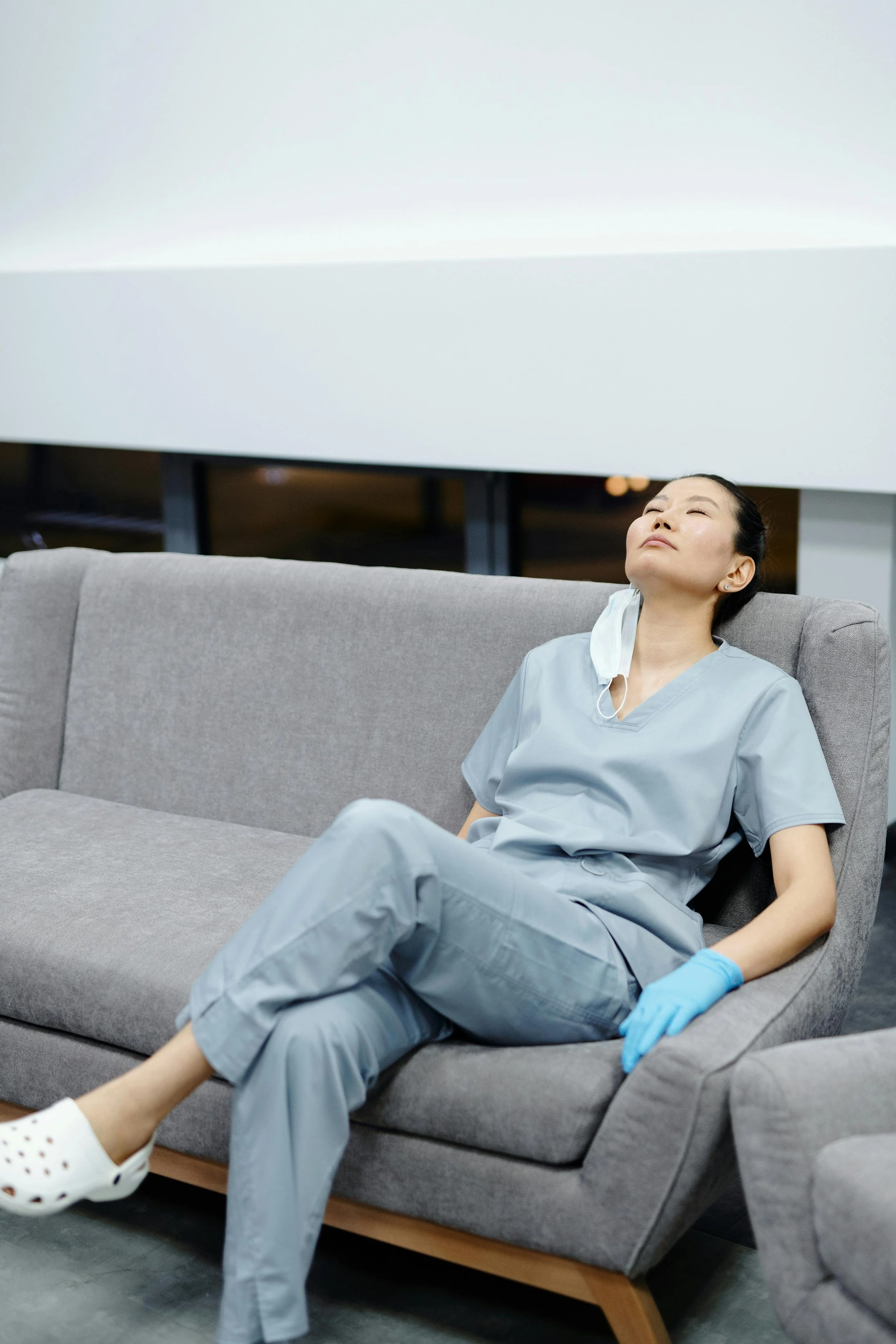 Person in scrubs lounging on a couch with head back and eyes closed, representing rest and recovery through therapy for helping professionals at Inside Out Therapy in Peoria Arizona