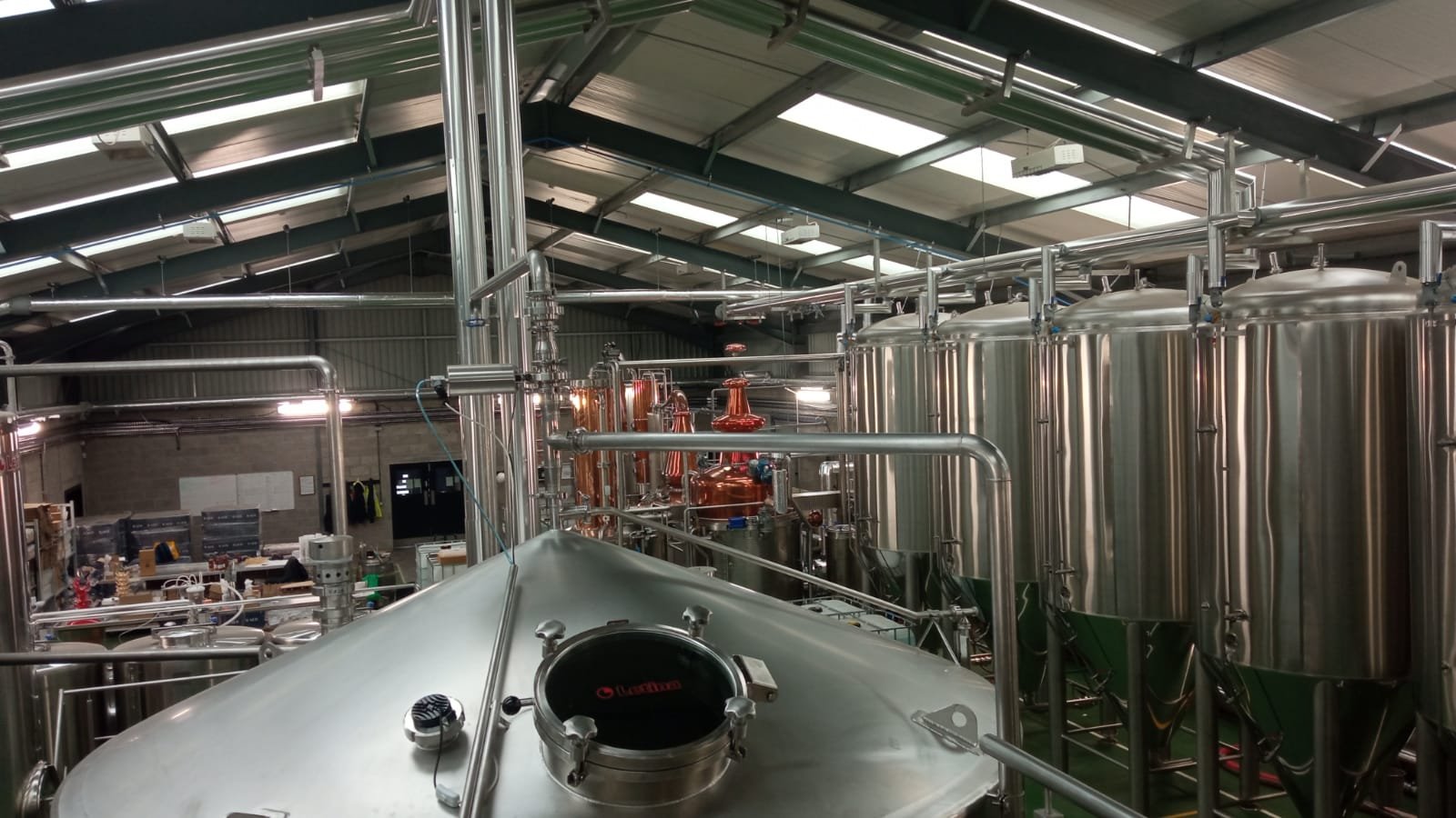 Interior view of a brewery with stainless steel fermentation tanks and brewing equipment in a large industrial space.