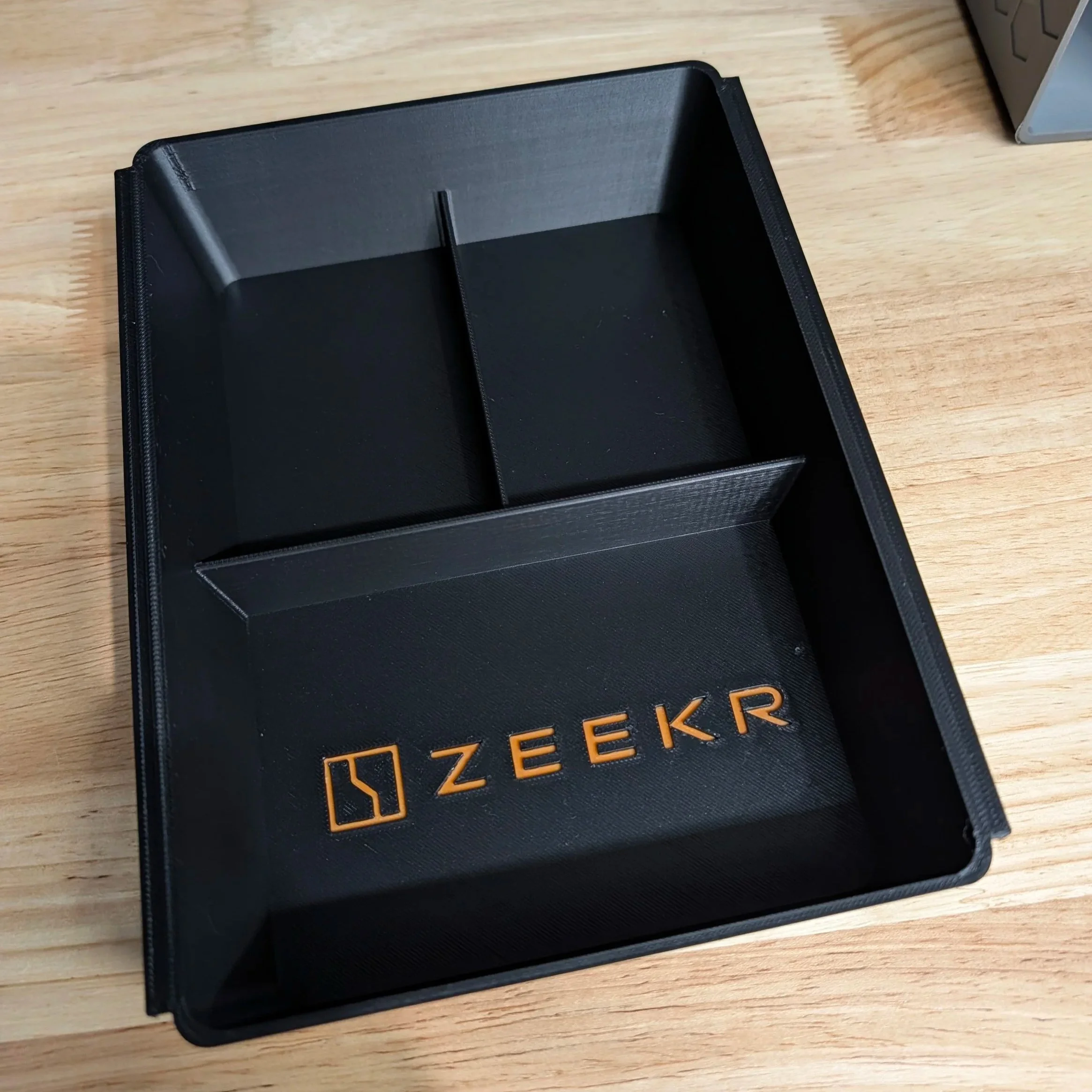 Empty black storage container with divided sections and the brand name 'ZEEKR' in orange letters inside.