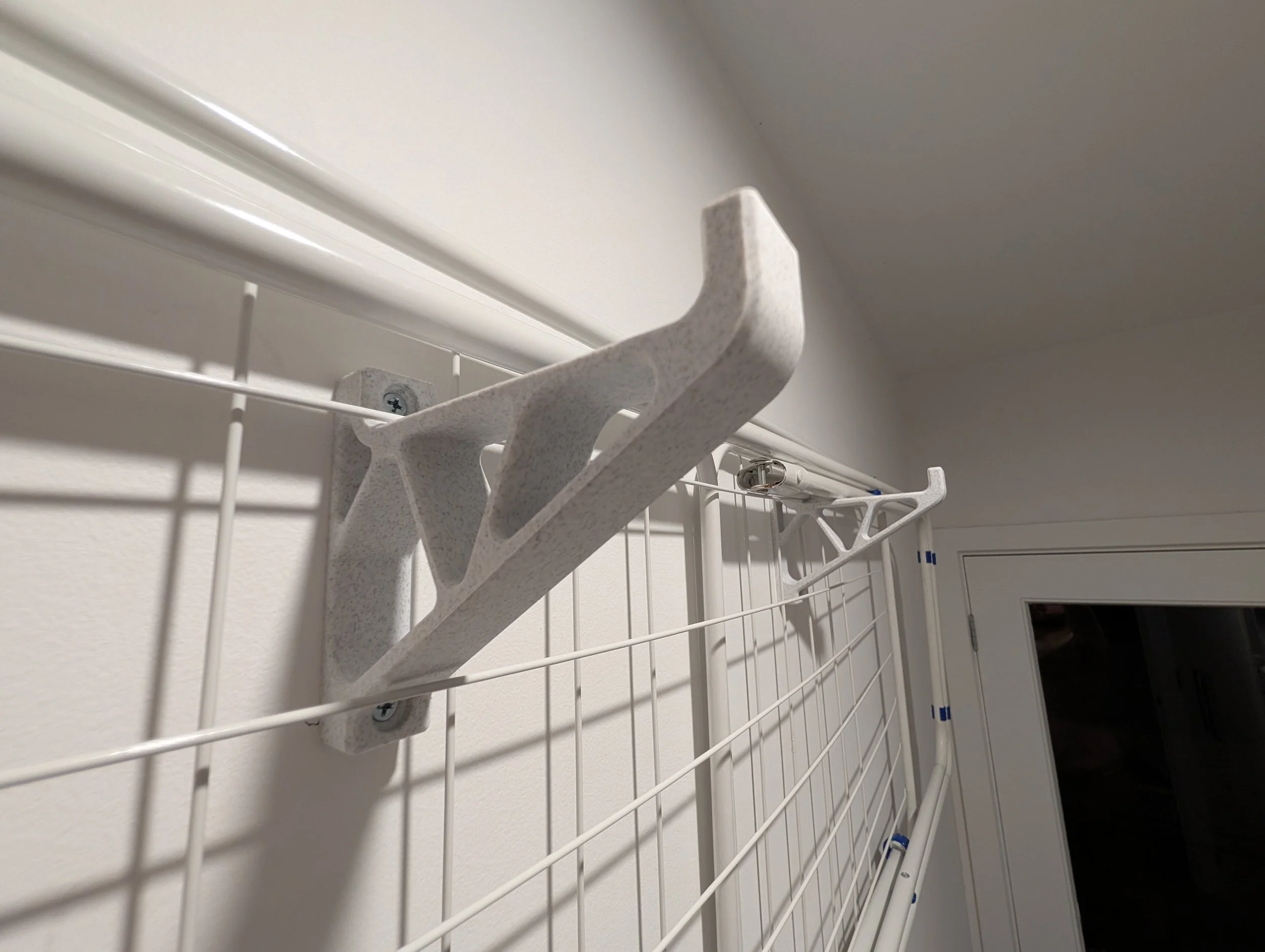 Close-up of a white wall-mounted drying rack with wire grids, fastened to a wall with screws, next to a door with a window.
