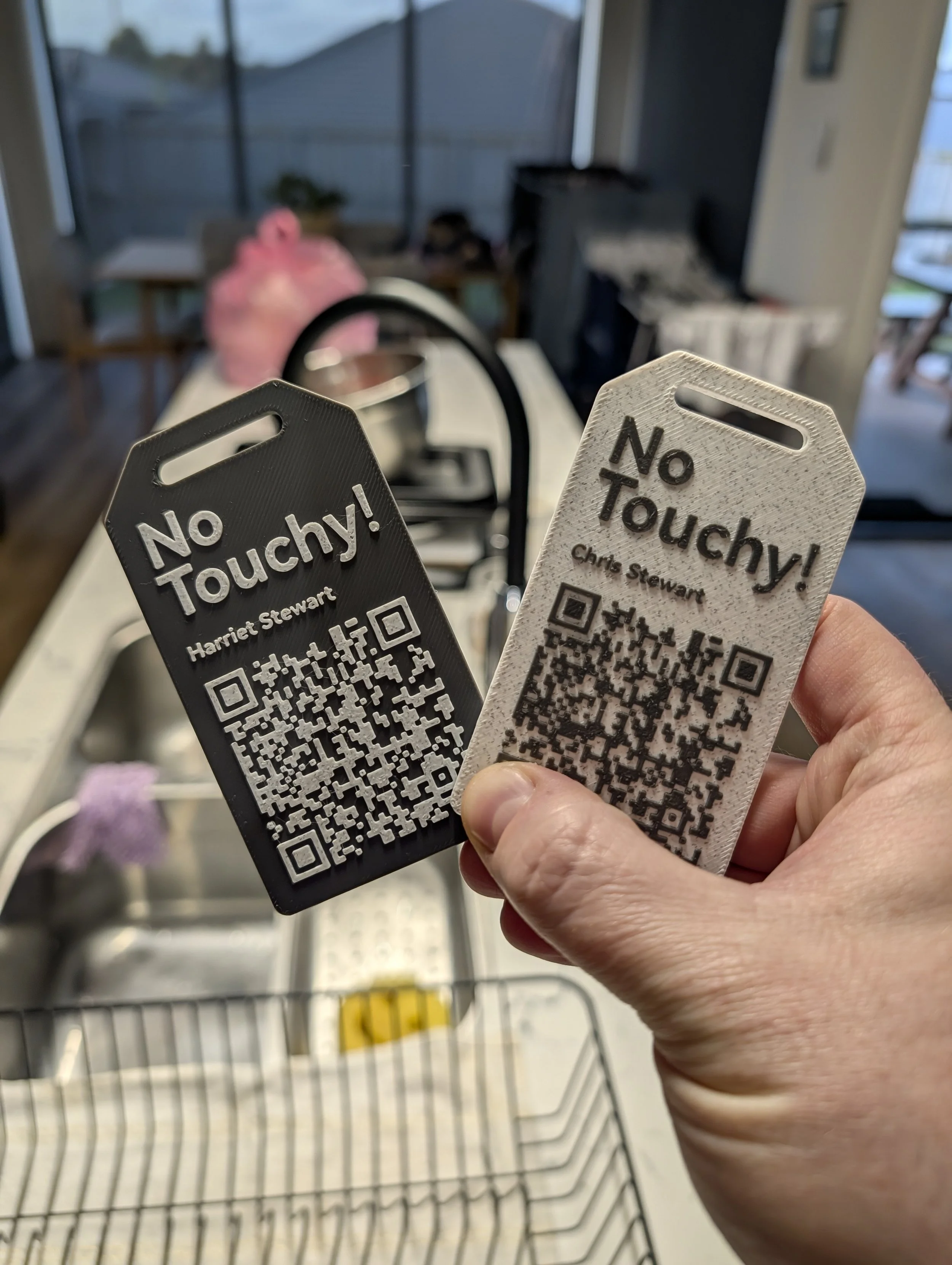 Two anti-touch tags labeled 'No Touchy!' with QR codes, held in a person's hand over a kitchen sink.