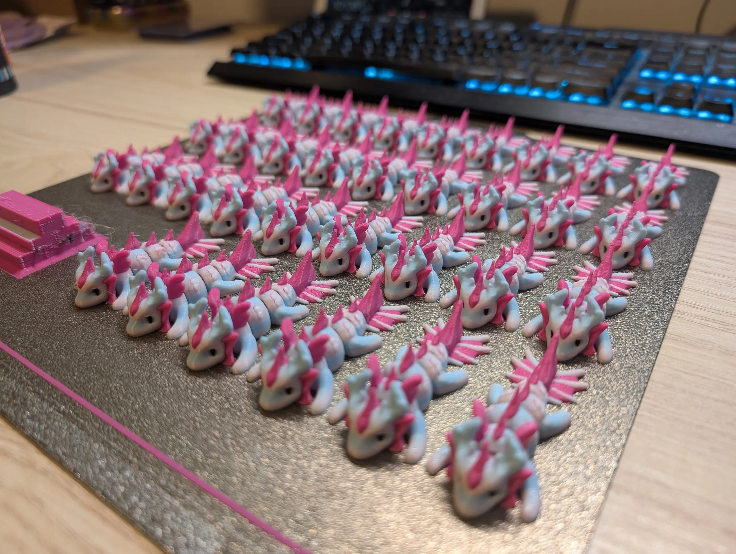 Numerous small pink and white unicorn figurines arranged neatly on a black textured mat on a wooden desk, with a computer keyboard in the background.