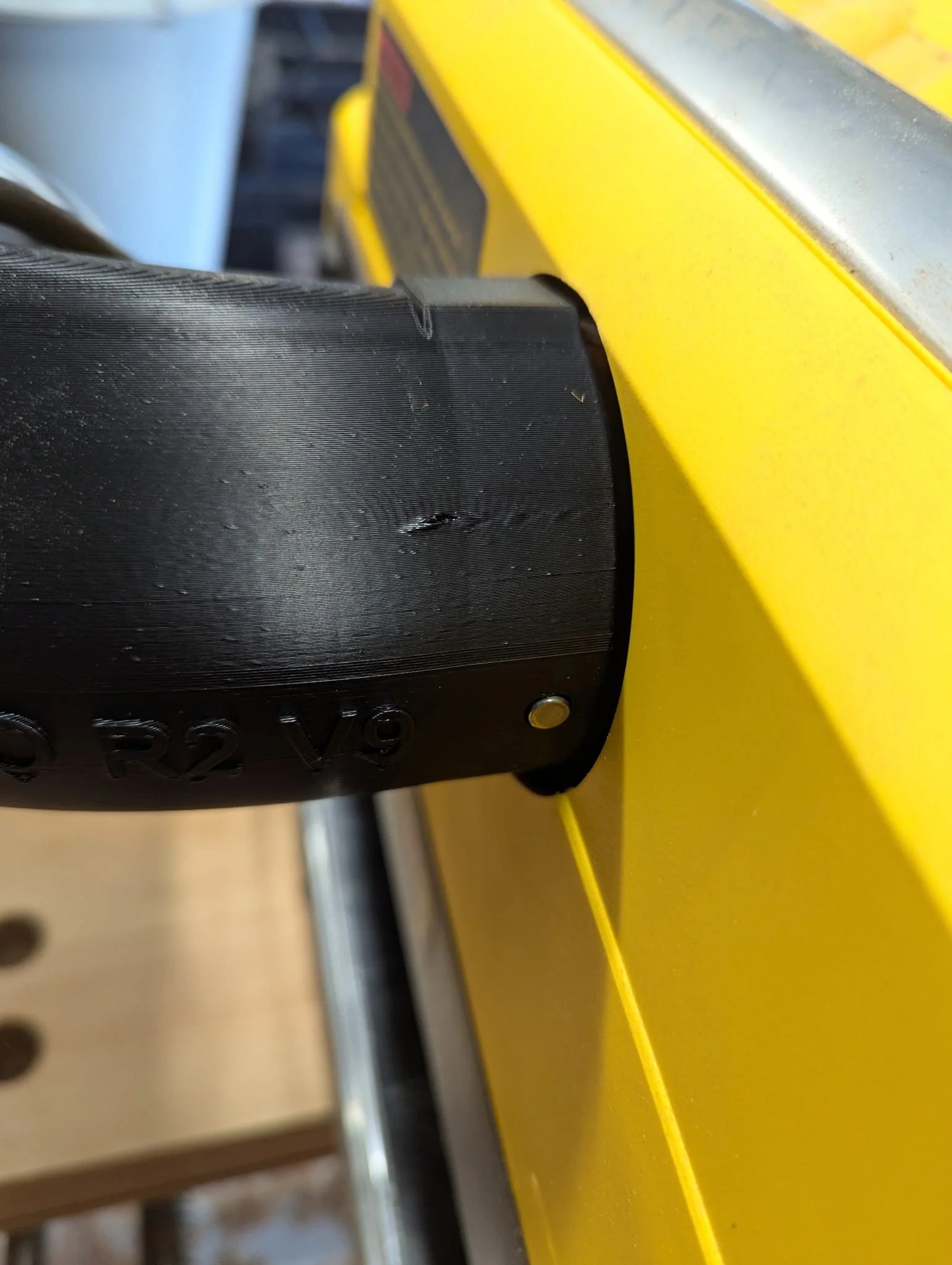 Close-up of a black plastic part attached to a yellow metallic surface, possibly part of a machinery or industrial equipment.