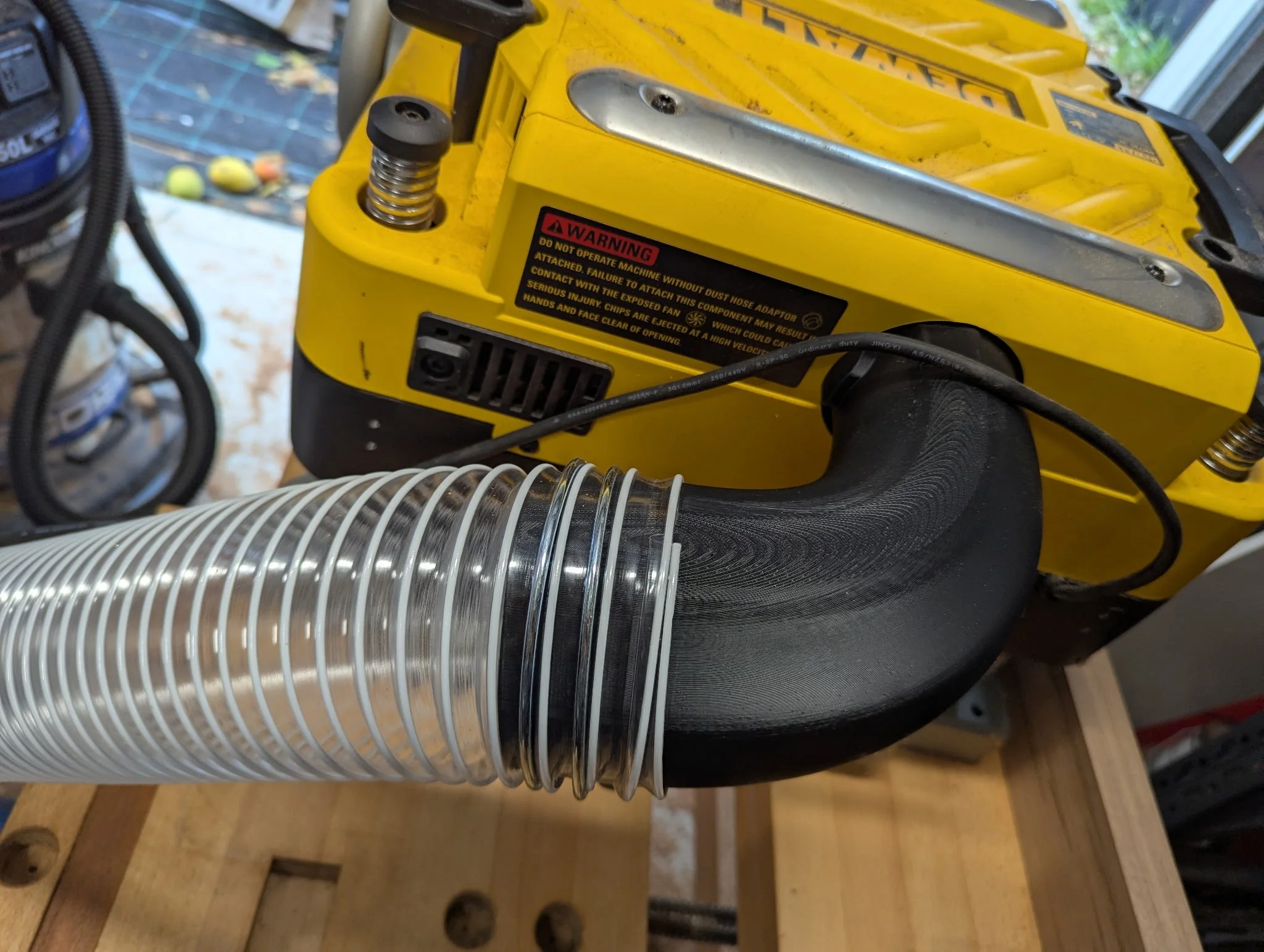A yellow industrial machine with a black exhaust pipe and a clear coiled hose connected to it, set on a wooden workbench.