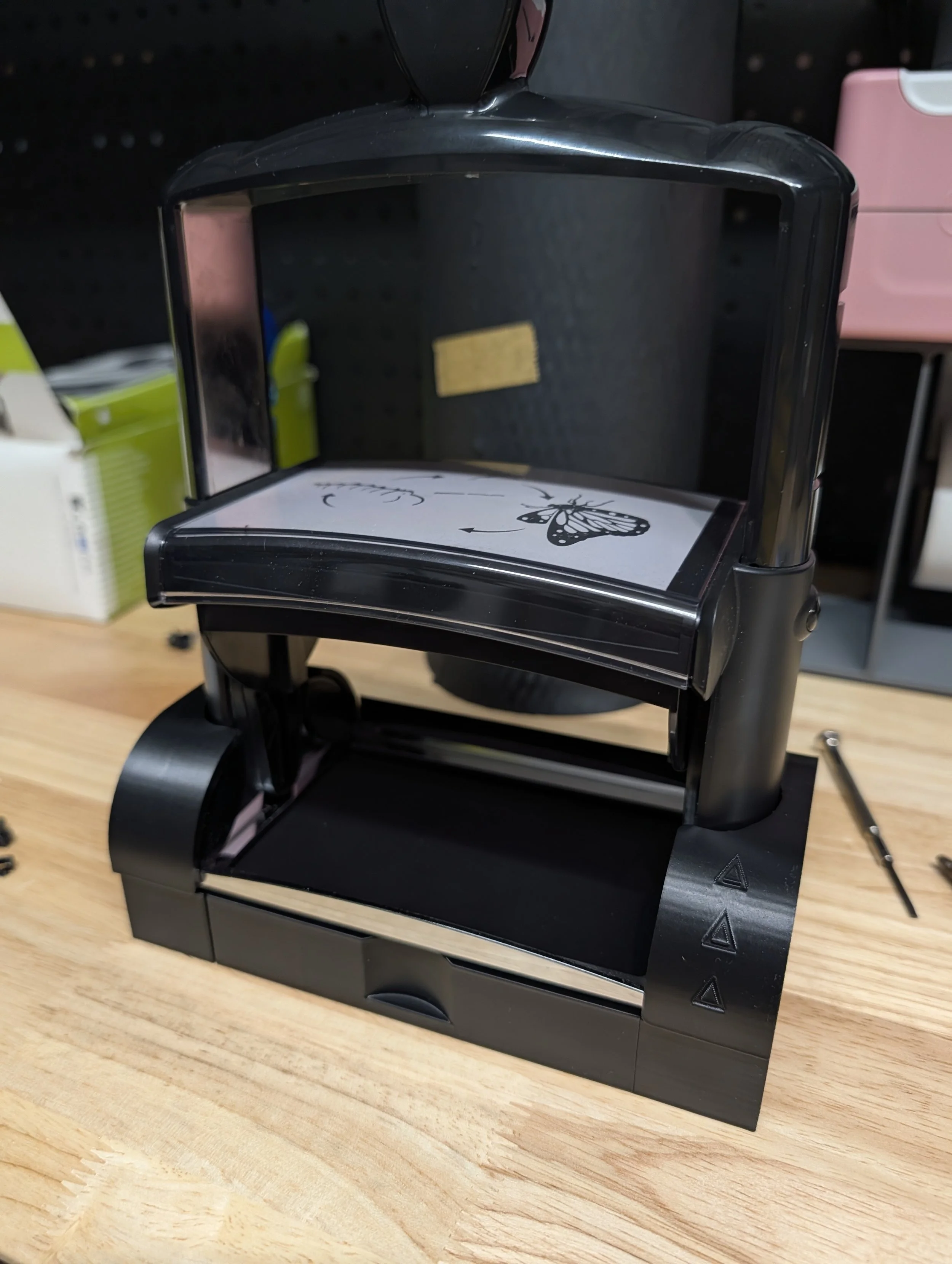 A black desktop 3D printer on a wooden workbench with an instruction sheet on top.