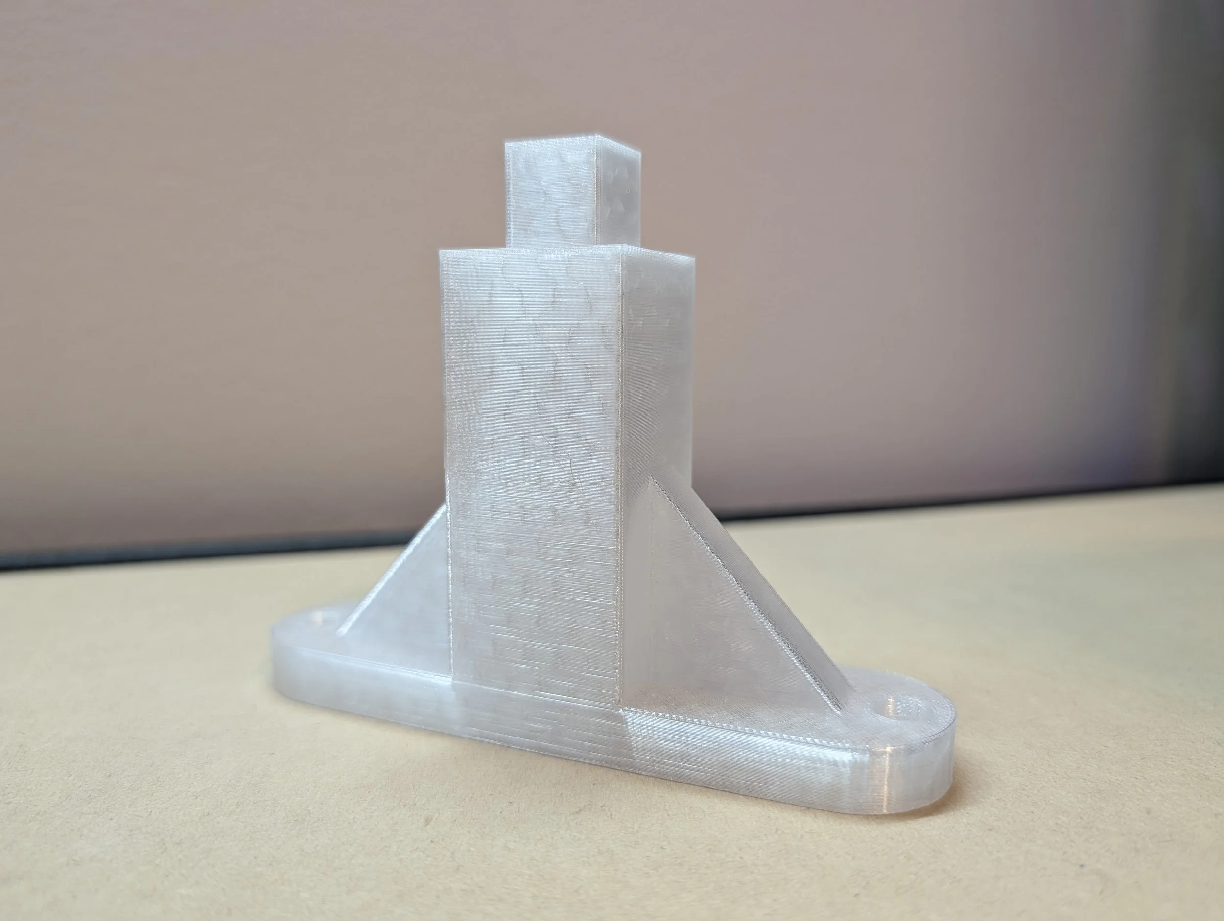 3D-printed transparent geometric sculpture with rectangular shapes and a base, placed on a beige surface with a plain background.