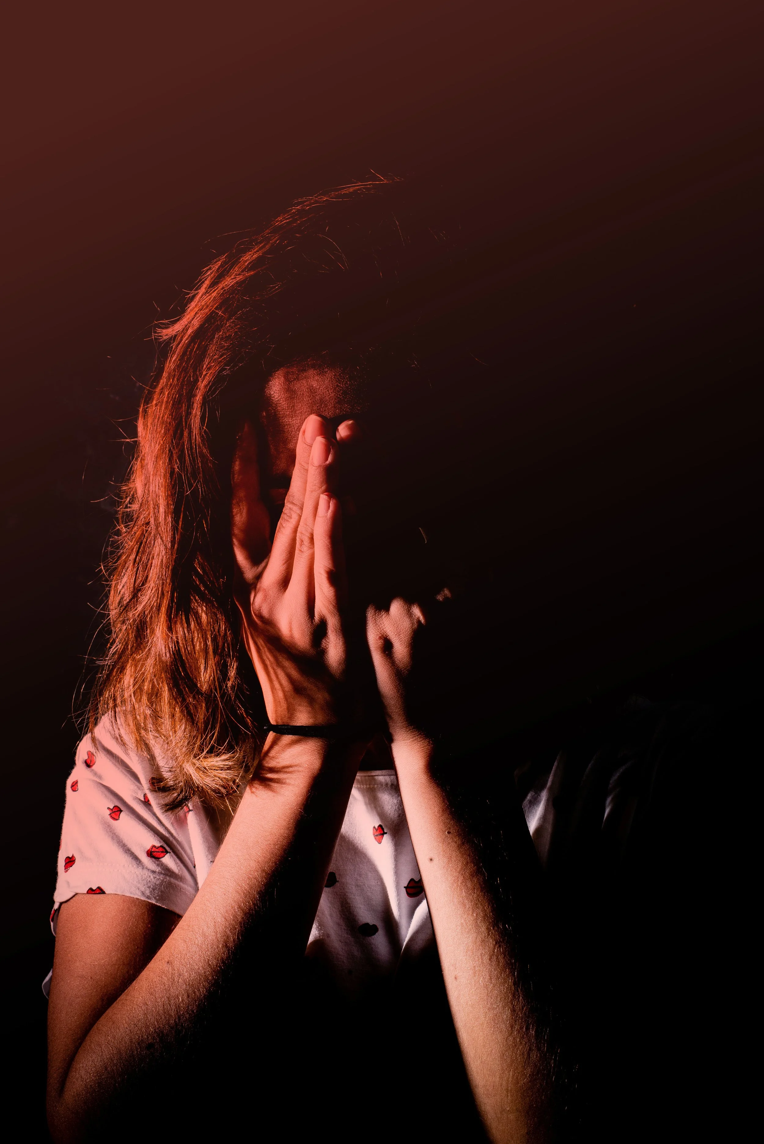 Gros plan sur une femme se couvrant le visage avec ses mains, éclairée par une lumière dramatique. Cette image symbolise le sentiment d'être submergée par les émotions, l'anxiété ou les doutes qu'un accompagnement en hypnose peut aider à transformer.