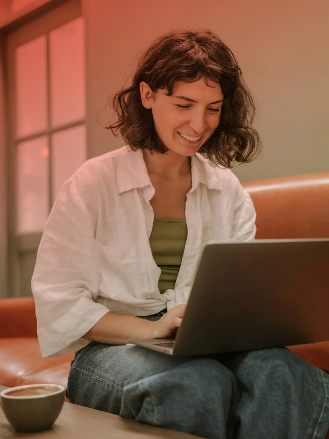 une femme sereine et souriante assise sur un canapé en cuir, utilisant son ordinateur pour un appel vidéo. Ambiance chaleureuse et décontractée pour symboliser un premier contact gratuit et sans engagement avec une praticienne en hypnose.