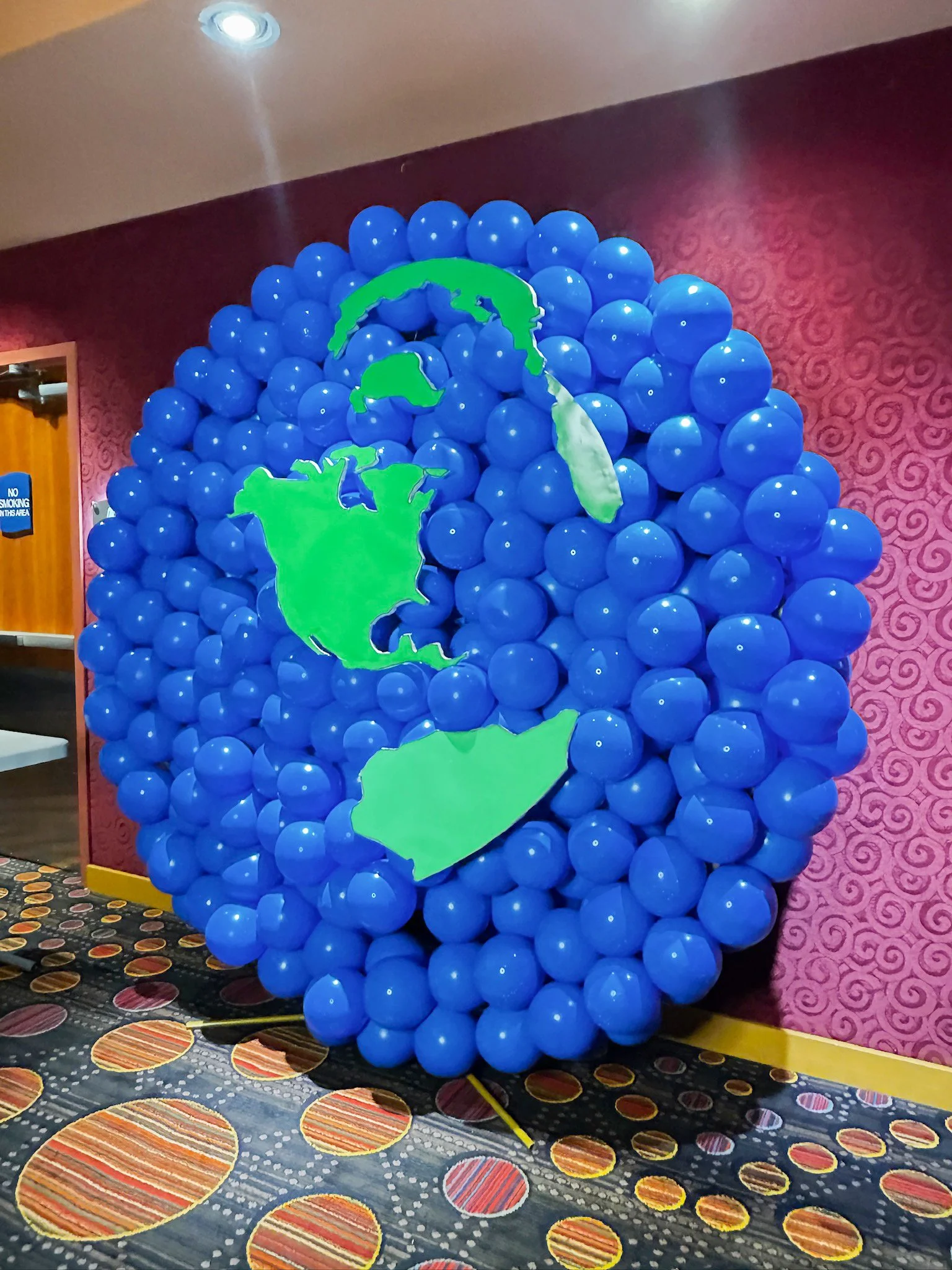 Display made of blue balloons with green cutouts of North America and South America, arranged to form a globe.