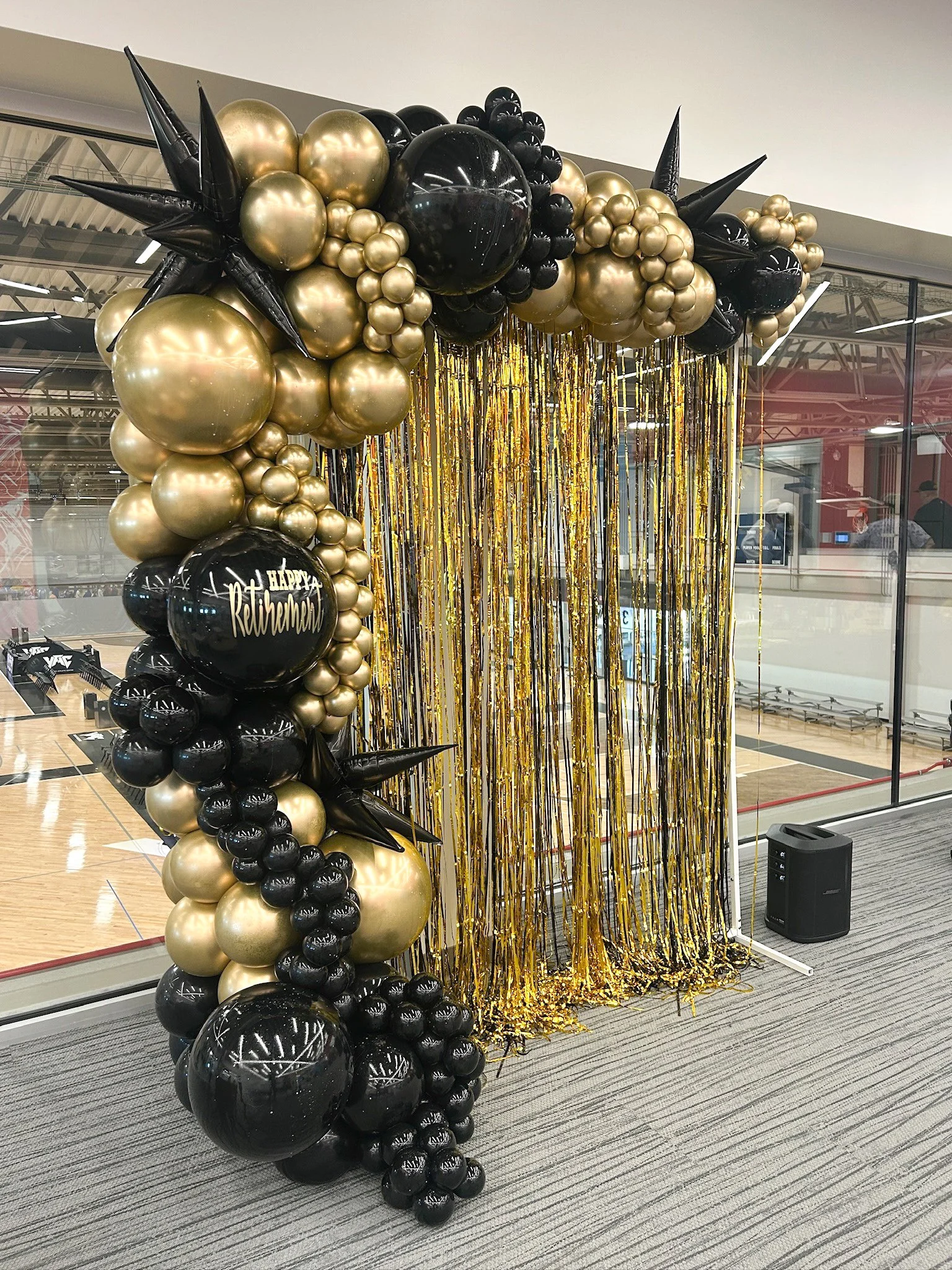 Black and gold balloon arch decoration with a hanging gold and black streamers backdrop, highlighting a birthday celebration for Rethanda.