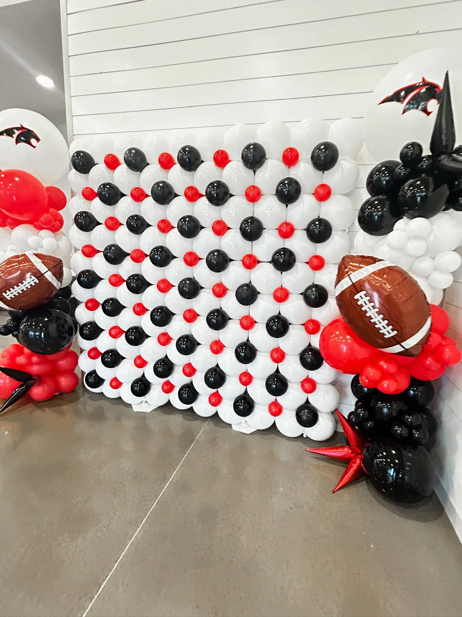A decorative balloon display featuring a wall of black, white, and red balloons, with NFL-themed balloons shaped like footballs, and star-shaped balloons in red and black, likely made for a sports celebration or party.