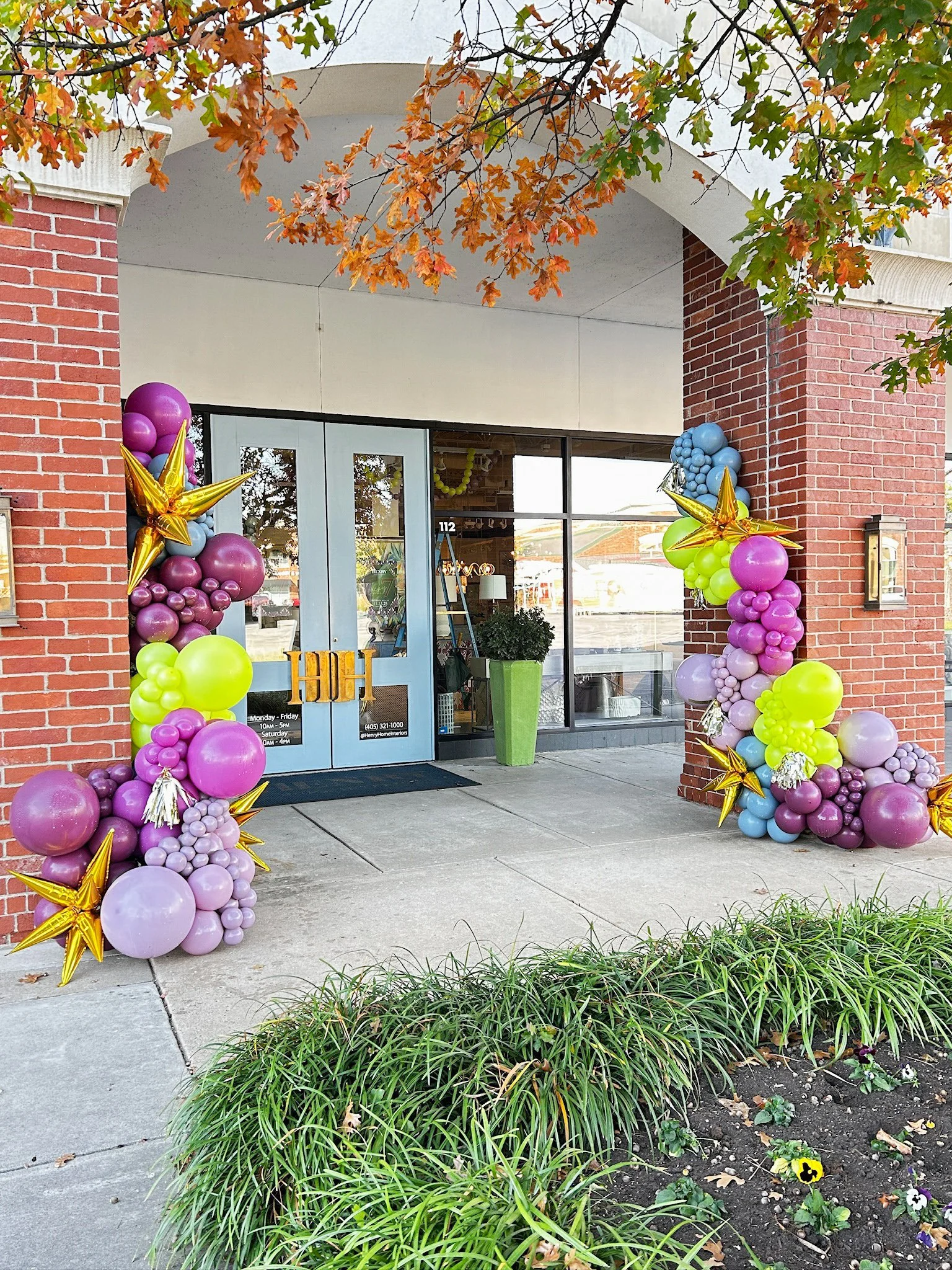 Decorative balloon arrangements in purple, yellow, green, blue, and lavender with gold star-shaped balloons framing the entrance of a building, decorated for a celebration or event.