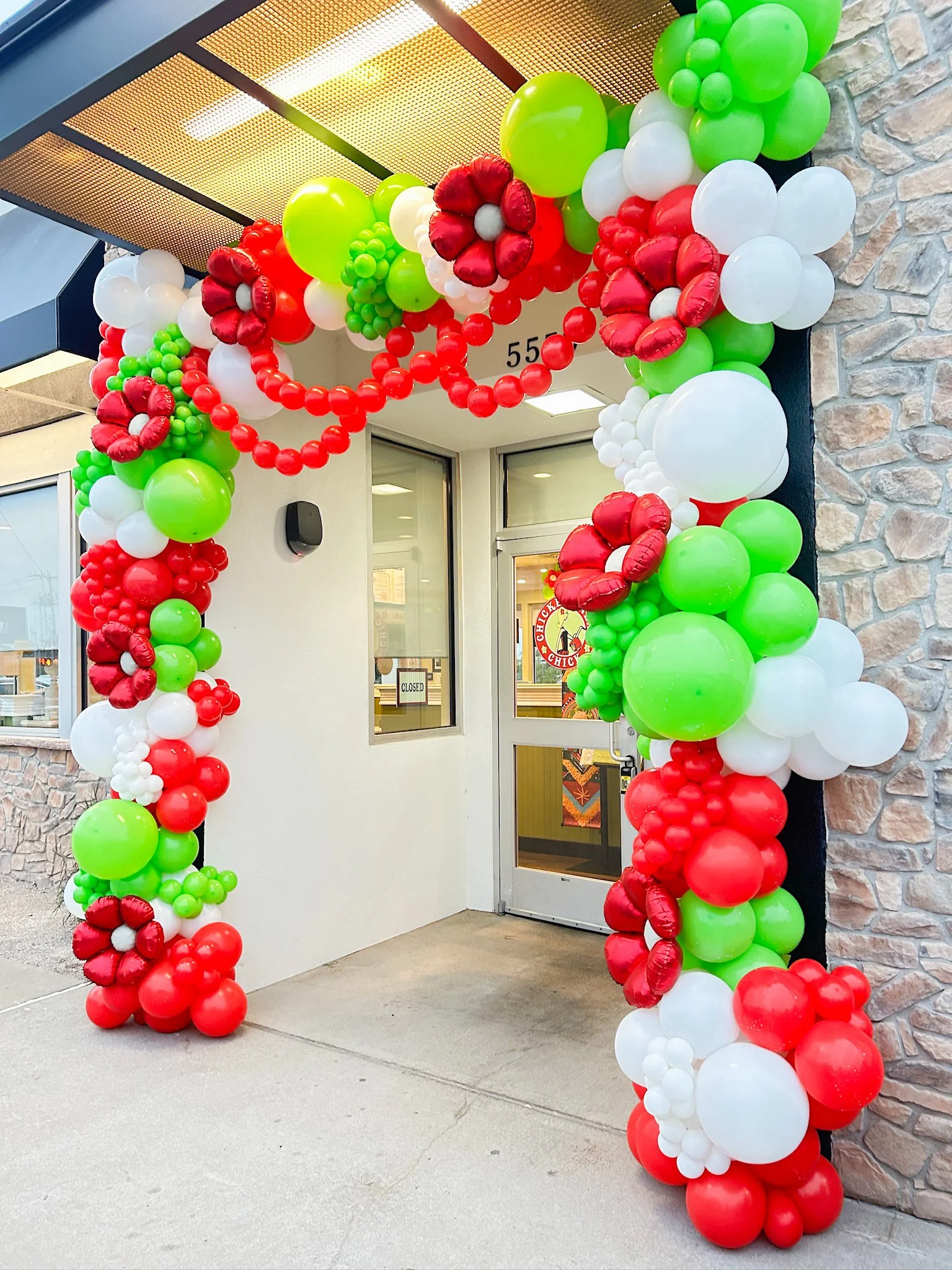 Decorative arch made of red, white, and green balloons, shaped with flowers and leaves, at the entrance of a building.