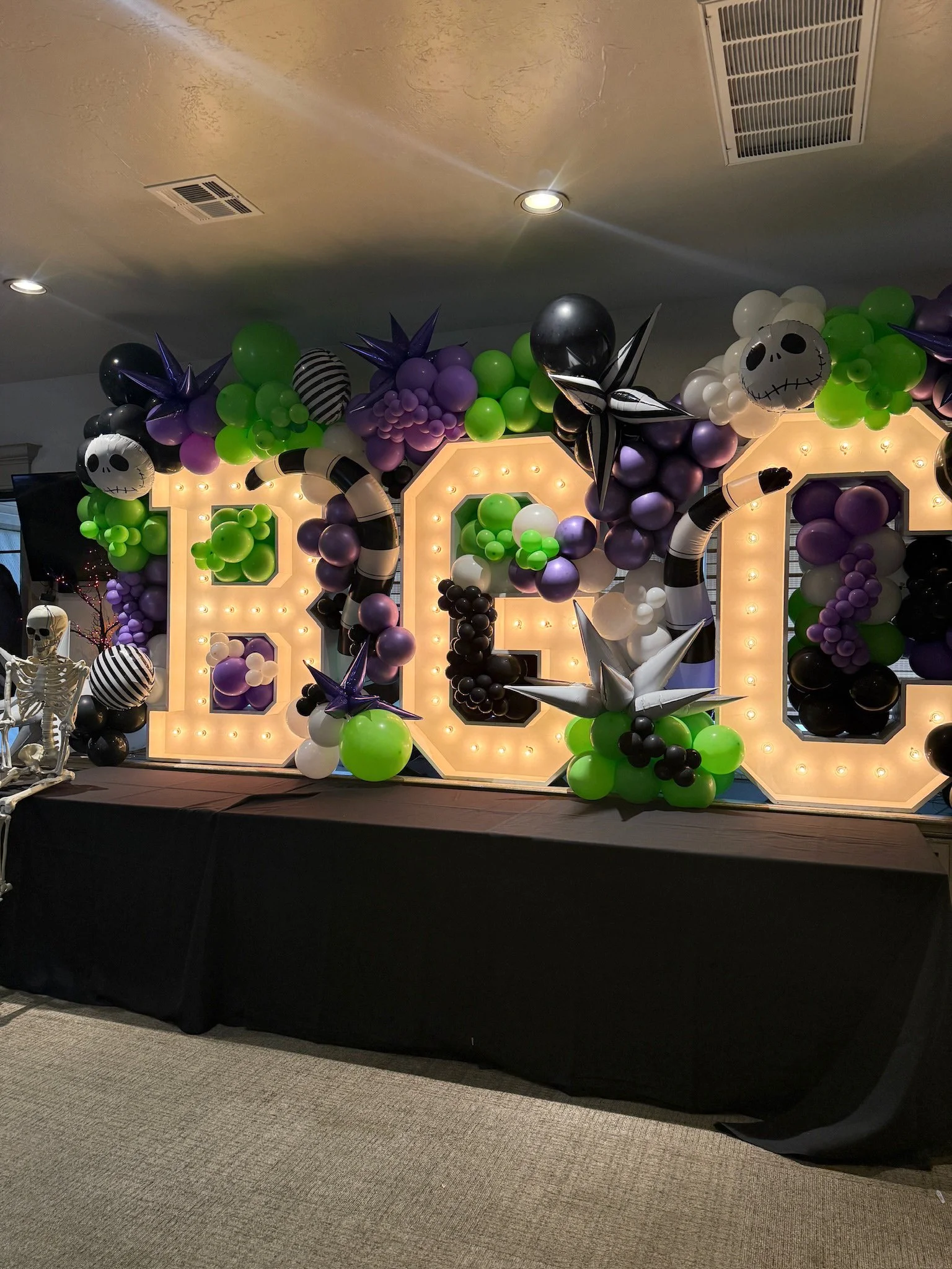 Decorative Halloween display with large illuminated letters spelling BORE, surrounded by colorful balloons, some with skull designs, and skeletons.