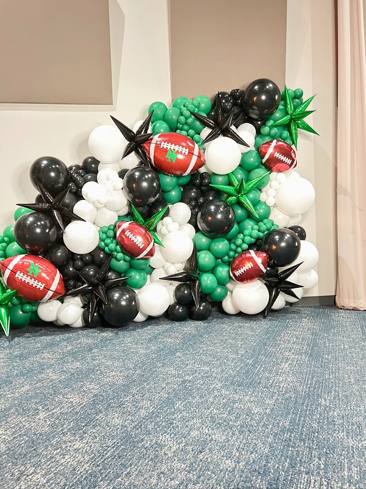 Balloon display with green, black, white, and football-shaped balloons, including some decorated with football patterns and team logos, arranged in a decorative cluster.