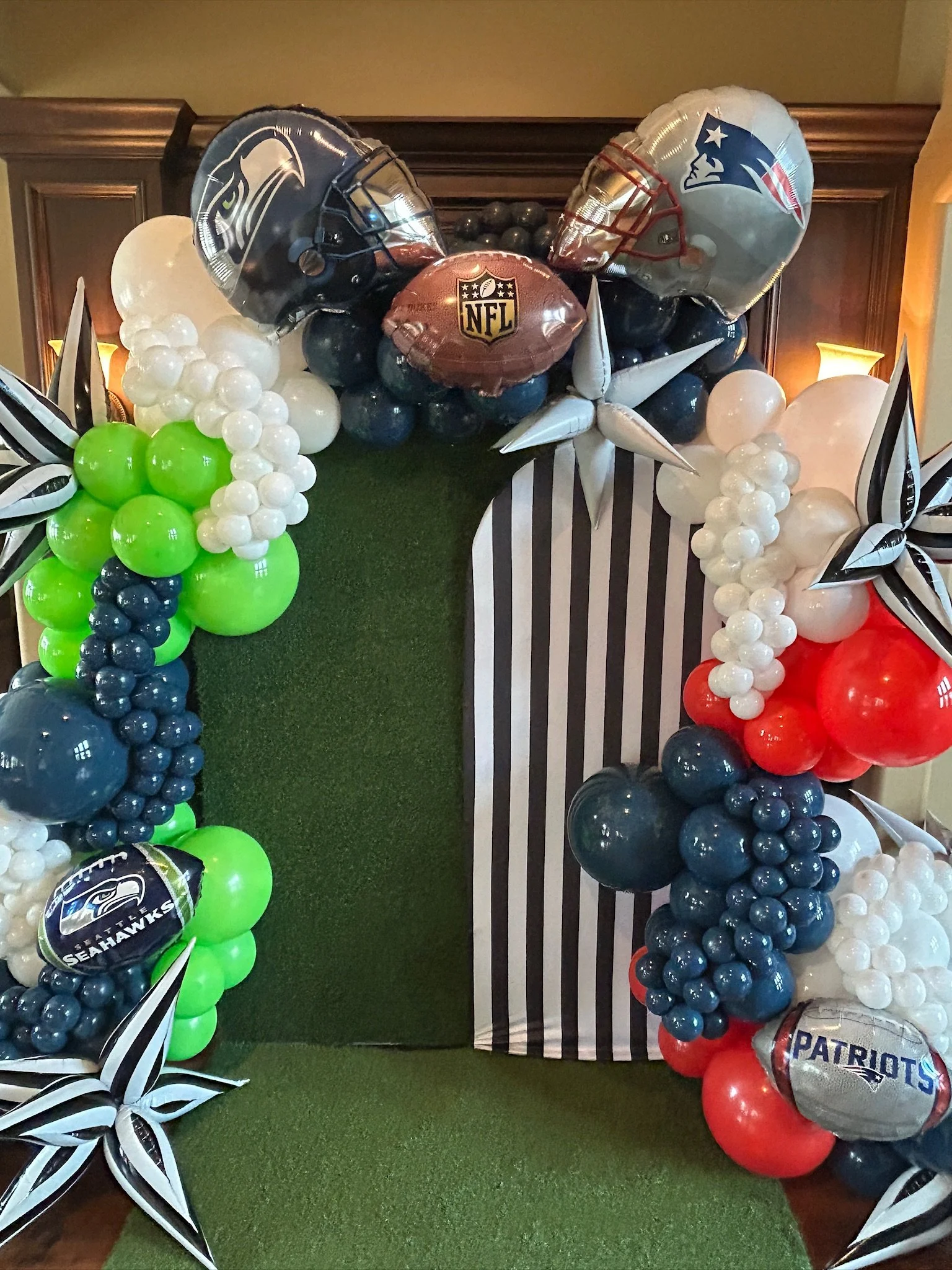 Football-themed balloon arrangement with NFL, Seahawks, Patriots logos, and star-shaped decorations in black, white, green, blue, red, and silver colors.
