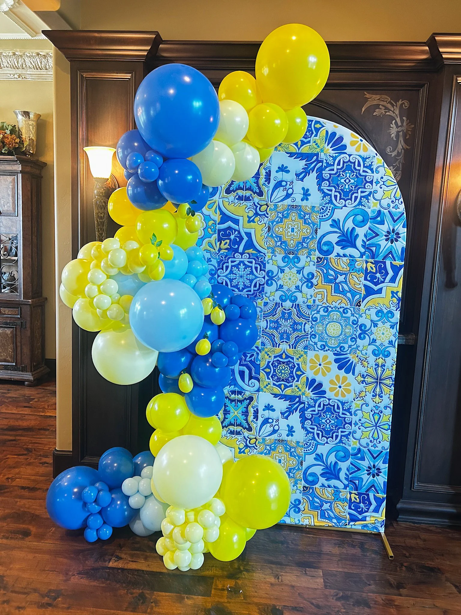 Colorful balloon arrangement in yellow, blue, white, and light blue in front of a blue and yellow tiled backdrop.