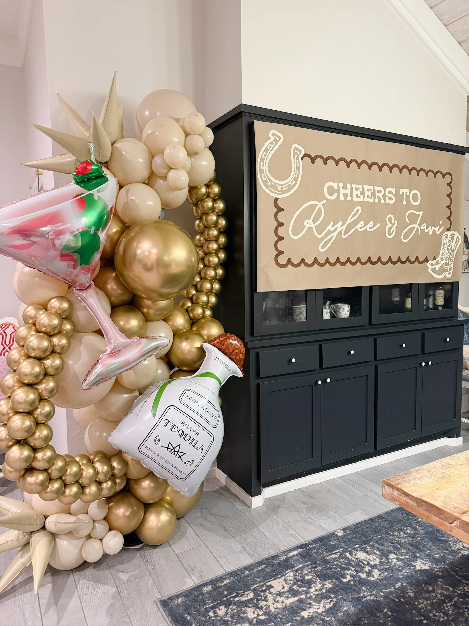 Decorative balloons and a sign with a cowboy hat and boot motifs celebrating Rylee and Javi. The balloons are mostly gold and white, with some shaped like cocktail glasses and a tequila bottle.