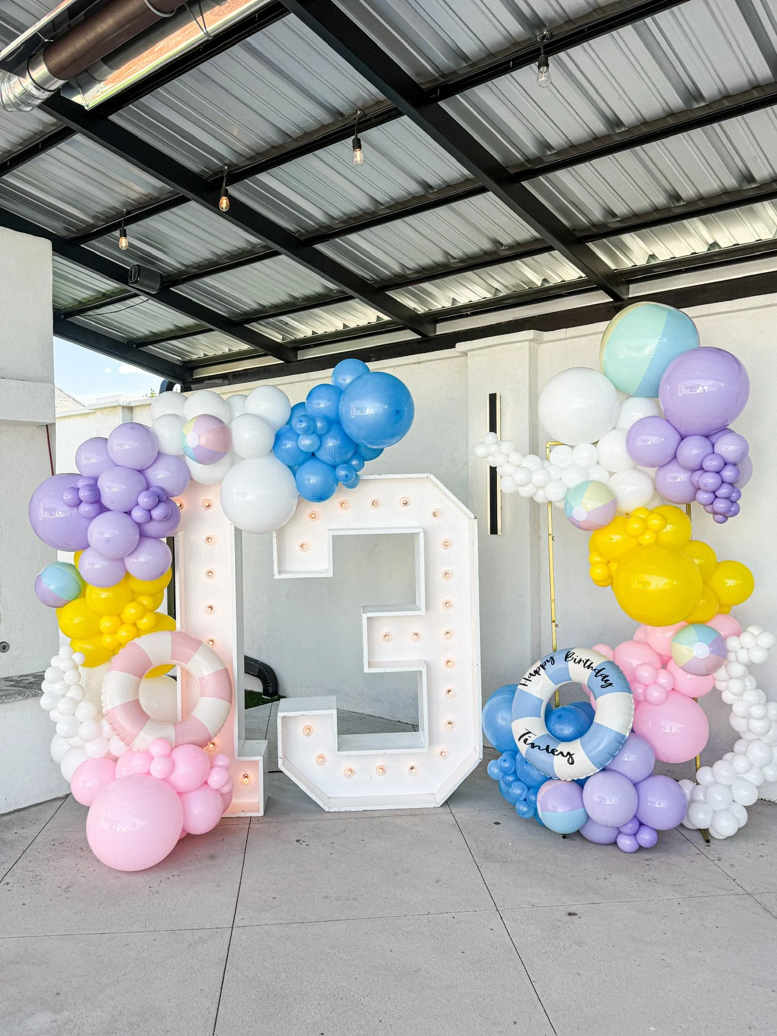 Decorative birthday balloon display with pastel-colored balloons surrounding a large illuminated number three.